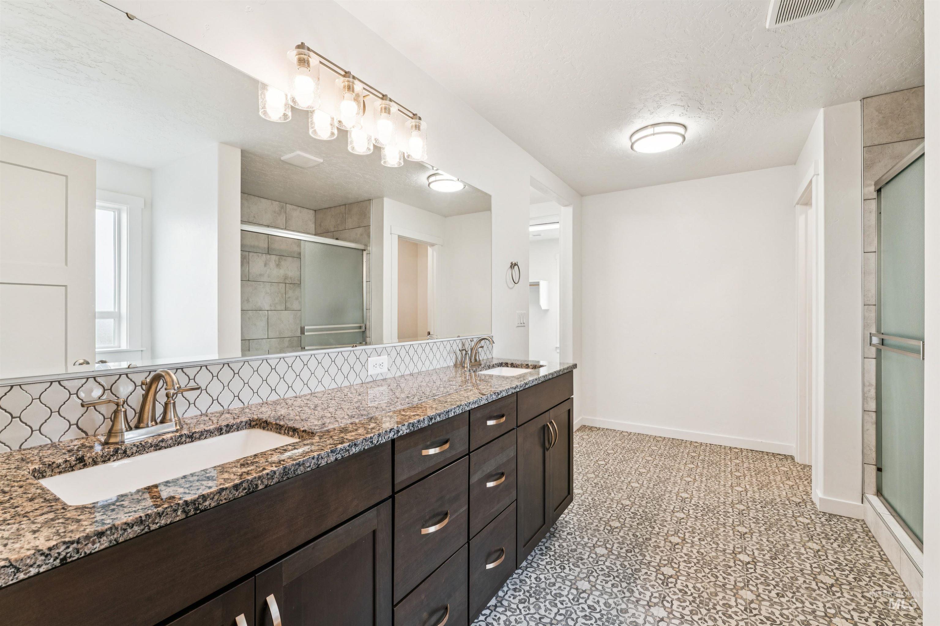 Bathroom featuring a textured ceiling, double vanity, and a stall shower