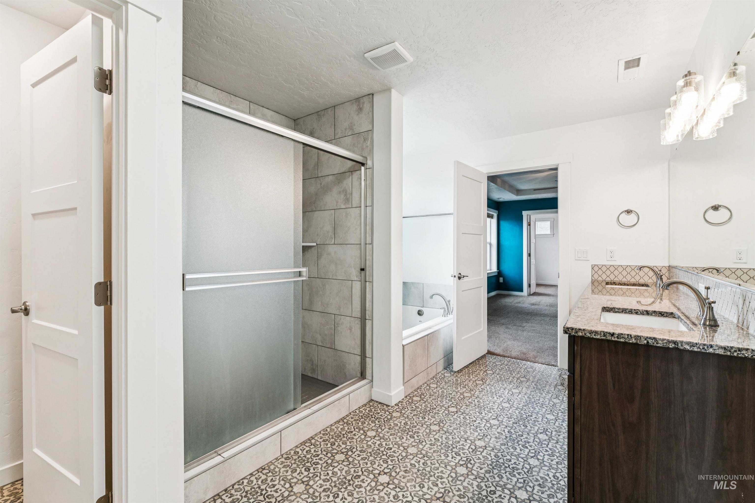 Full bath featuring a bath, double vanity, a textured ceiling, and a shower stall