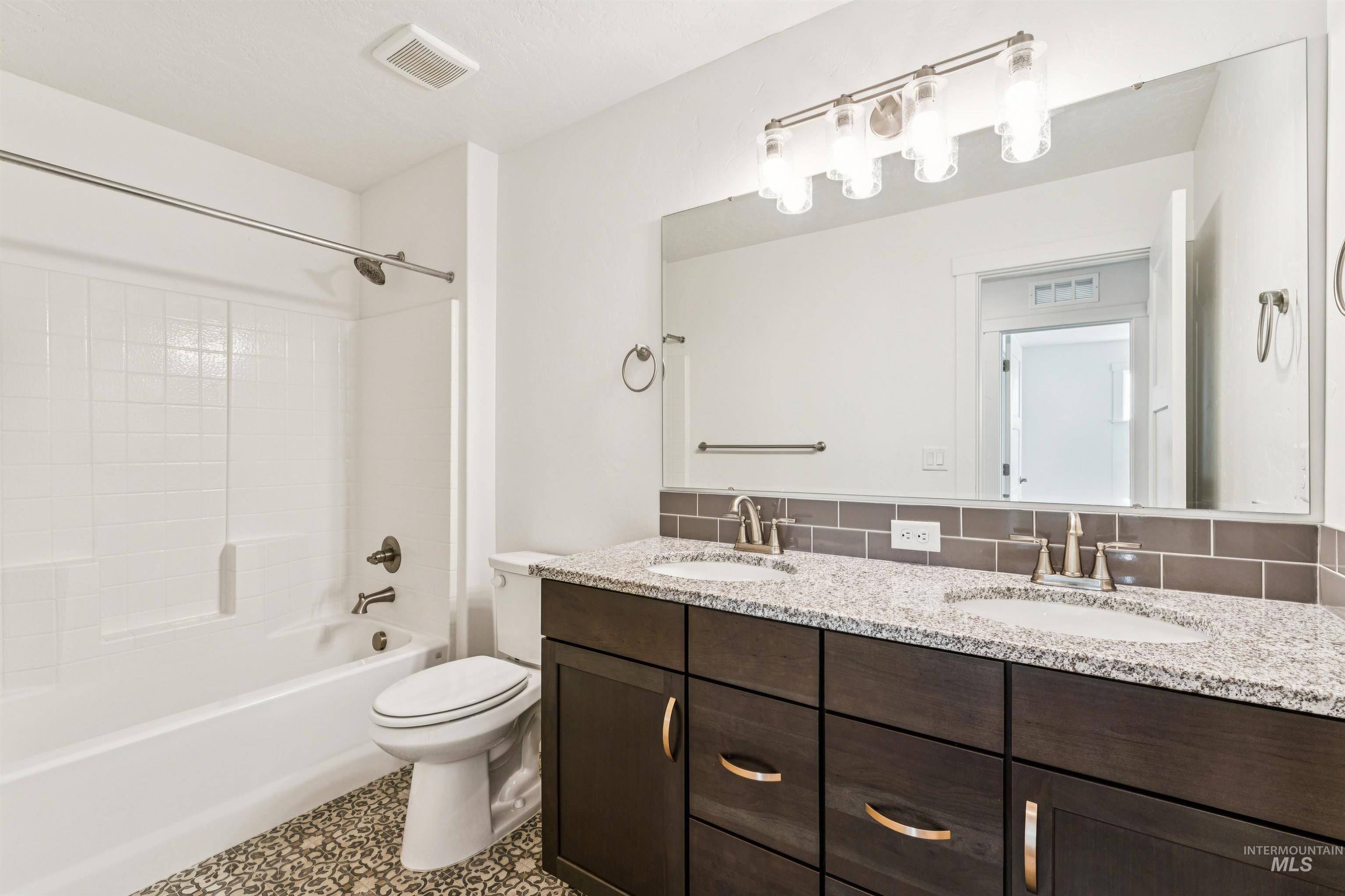 Full bath featuring double vanity, washtub / shower combination, and tasteful backsplash