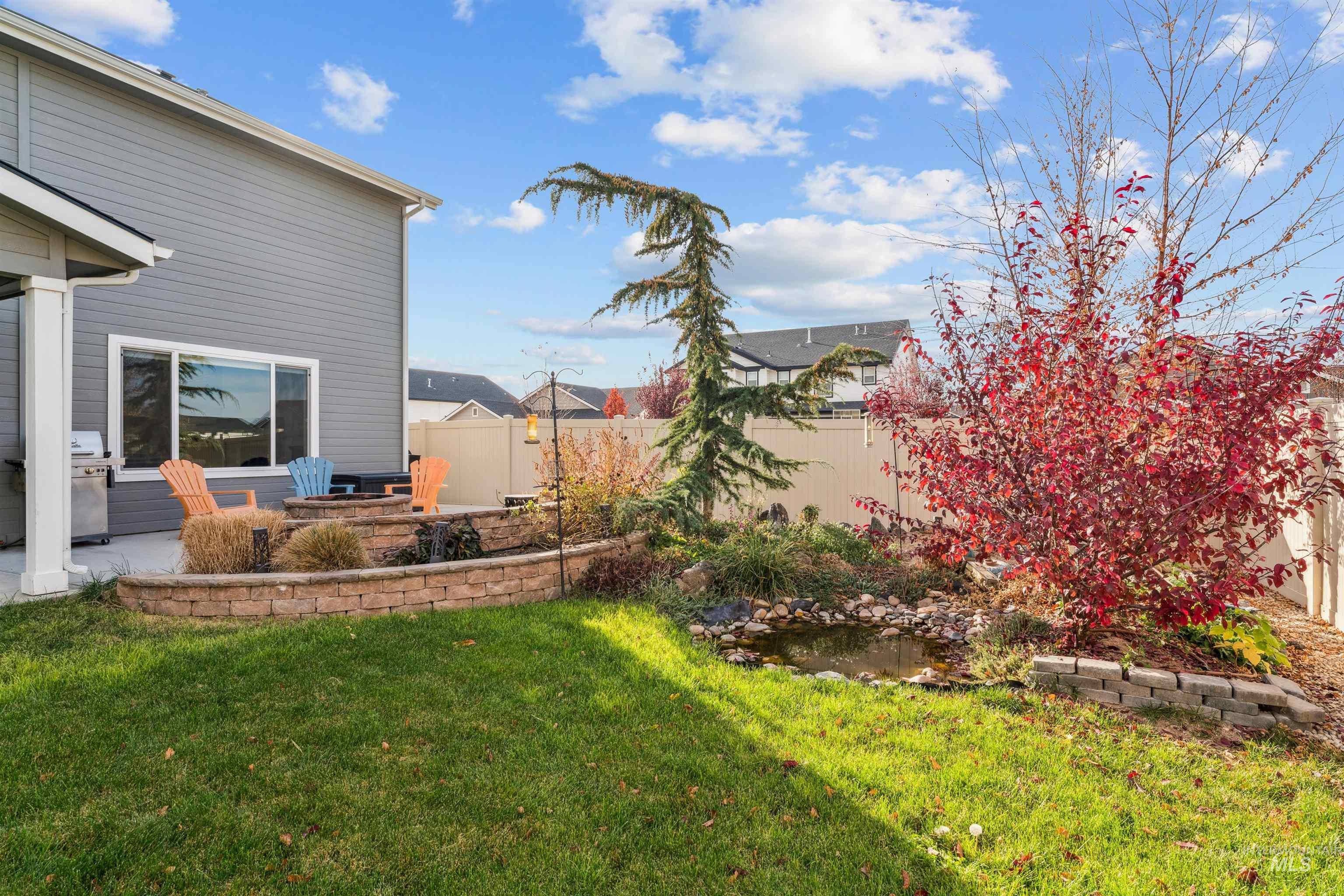 Fenced backyard with a garden pond, a patio area, and an outdoor fire pit