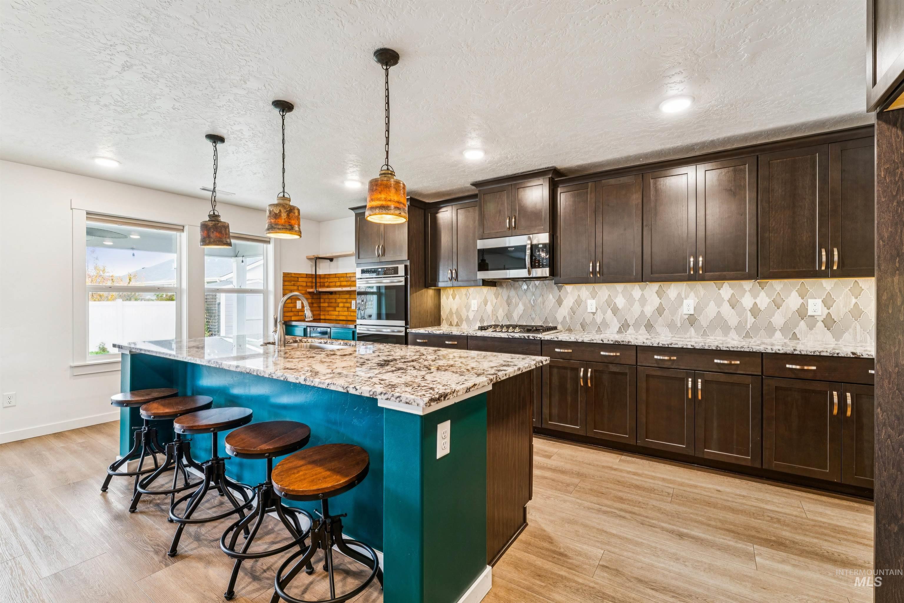 Kitchen with tasteful backsplash, dark brown cabinetry, a breakfast bar area, light stone counters, and a kitchen island with sink