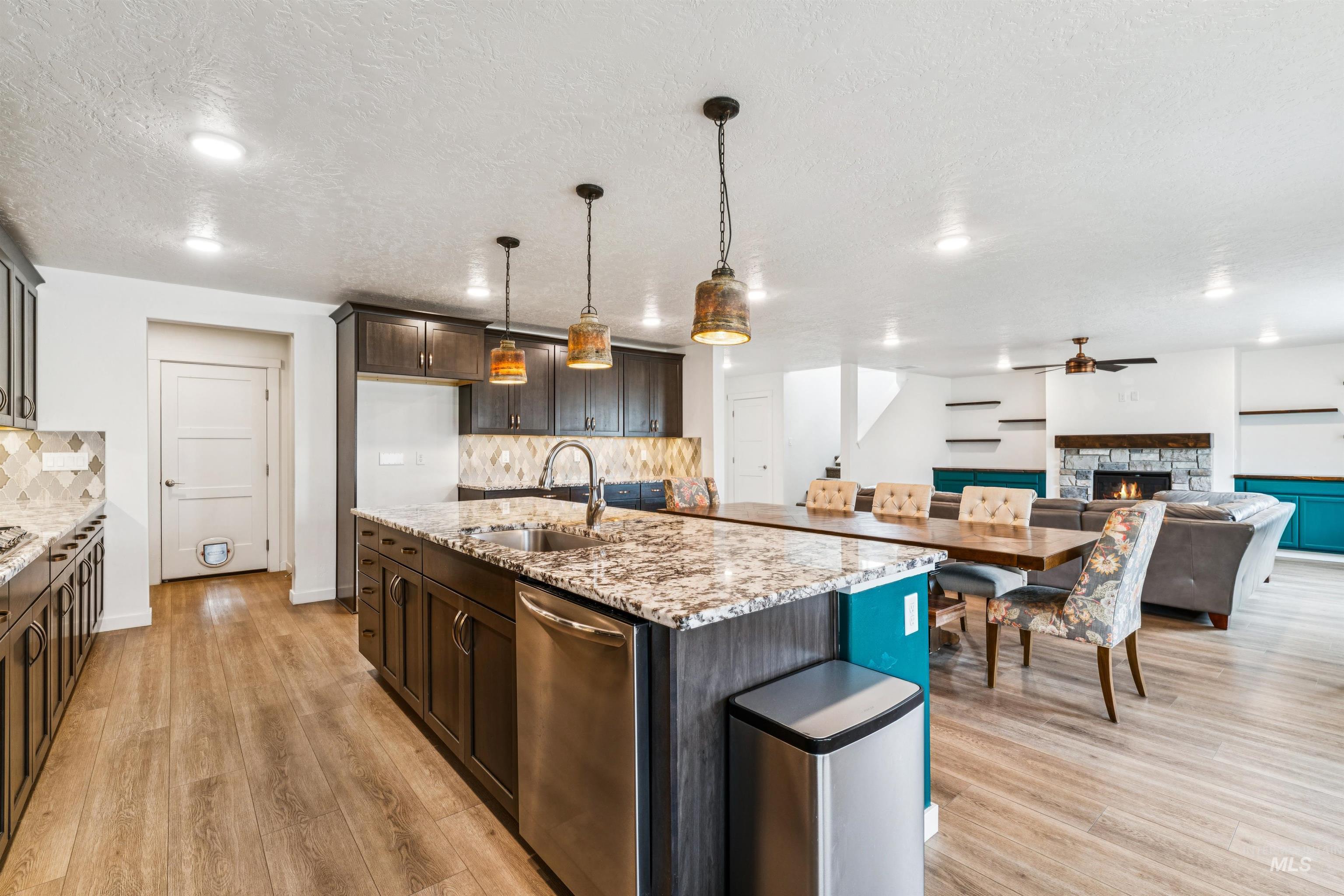 Kitchen with a fireplace, light stone countertops, hanging light fixtures, dishwasher, and dark brown cabinetry