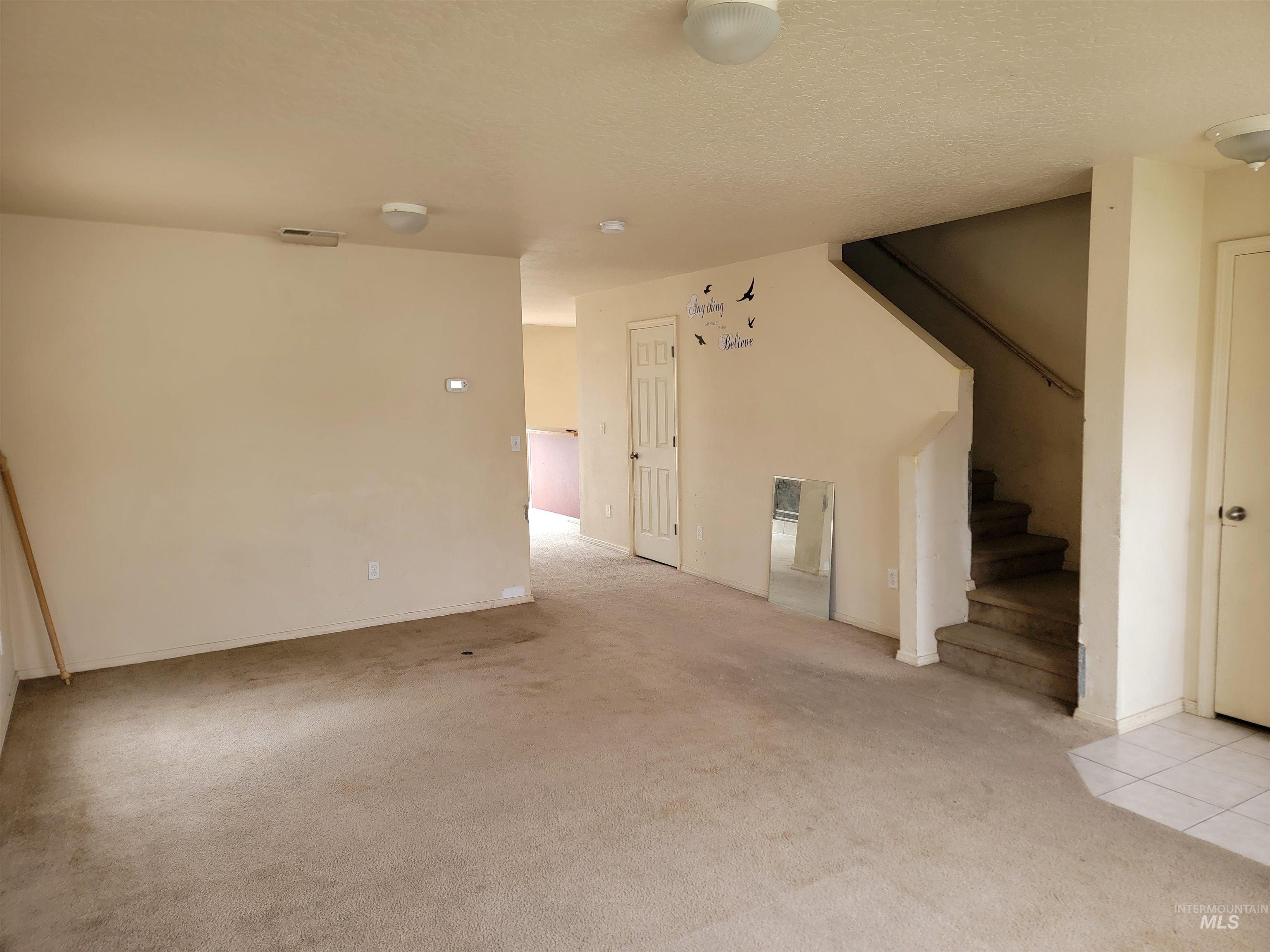 Unfurnished living room with stairway, light carpet, and a textured ceiling