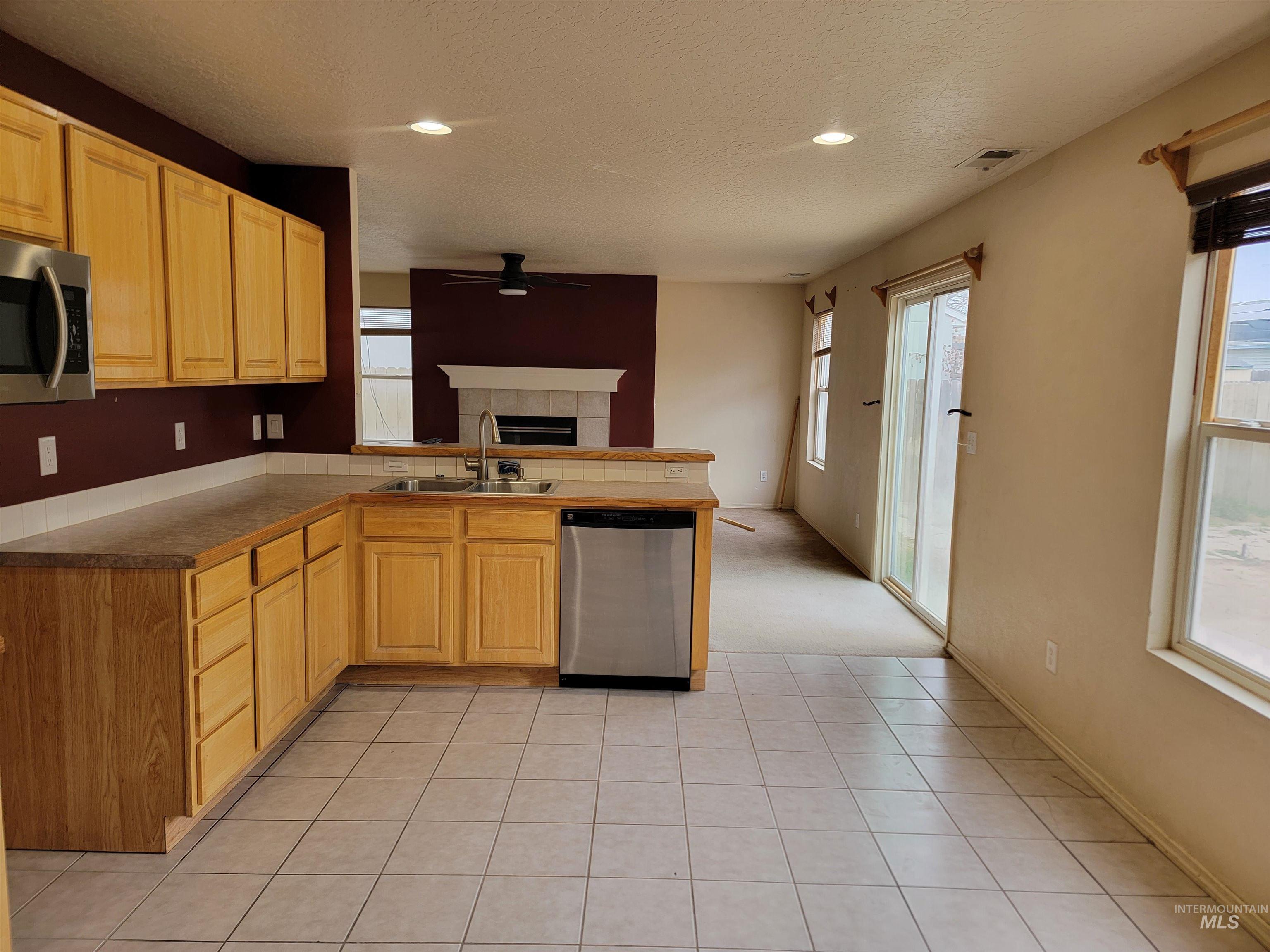 Kitchen with appliances with stainless steel finishes, a peninsula, a ceiling fan, light tile patterned floors, and a textured ceiling