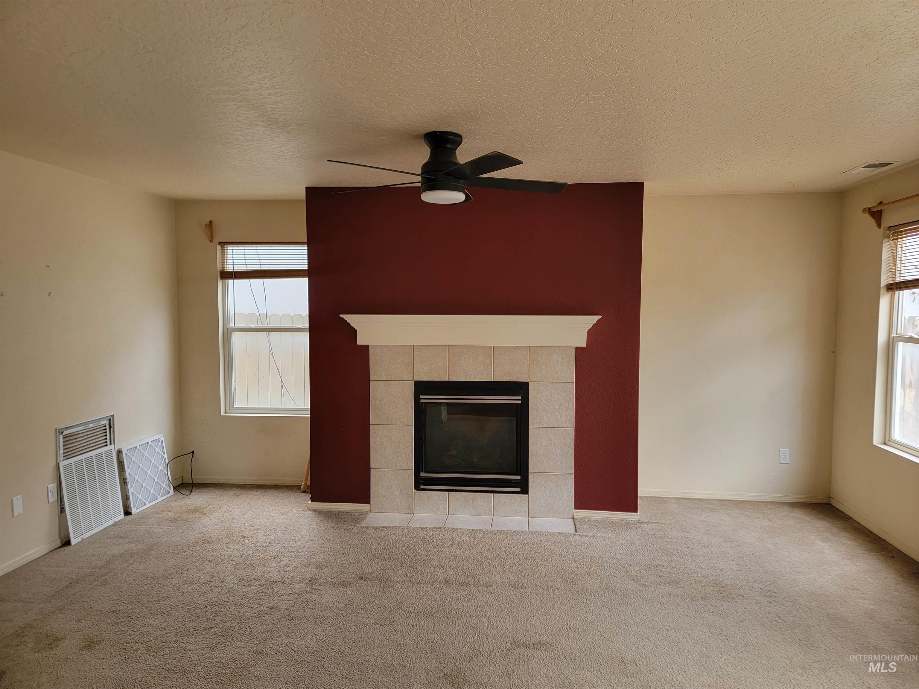 Unfurnished living room featuring a tiled fireplace, carpet, a textured ceiling, and a ceiling fan