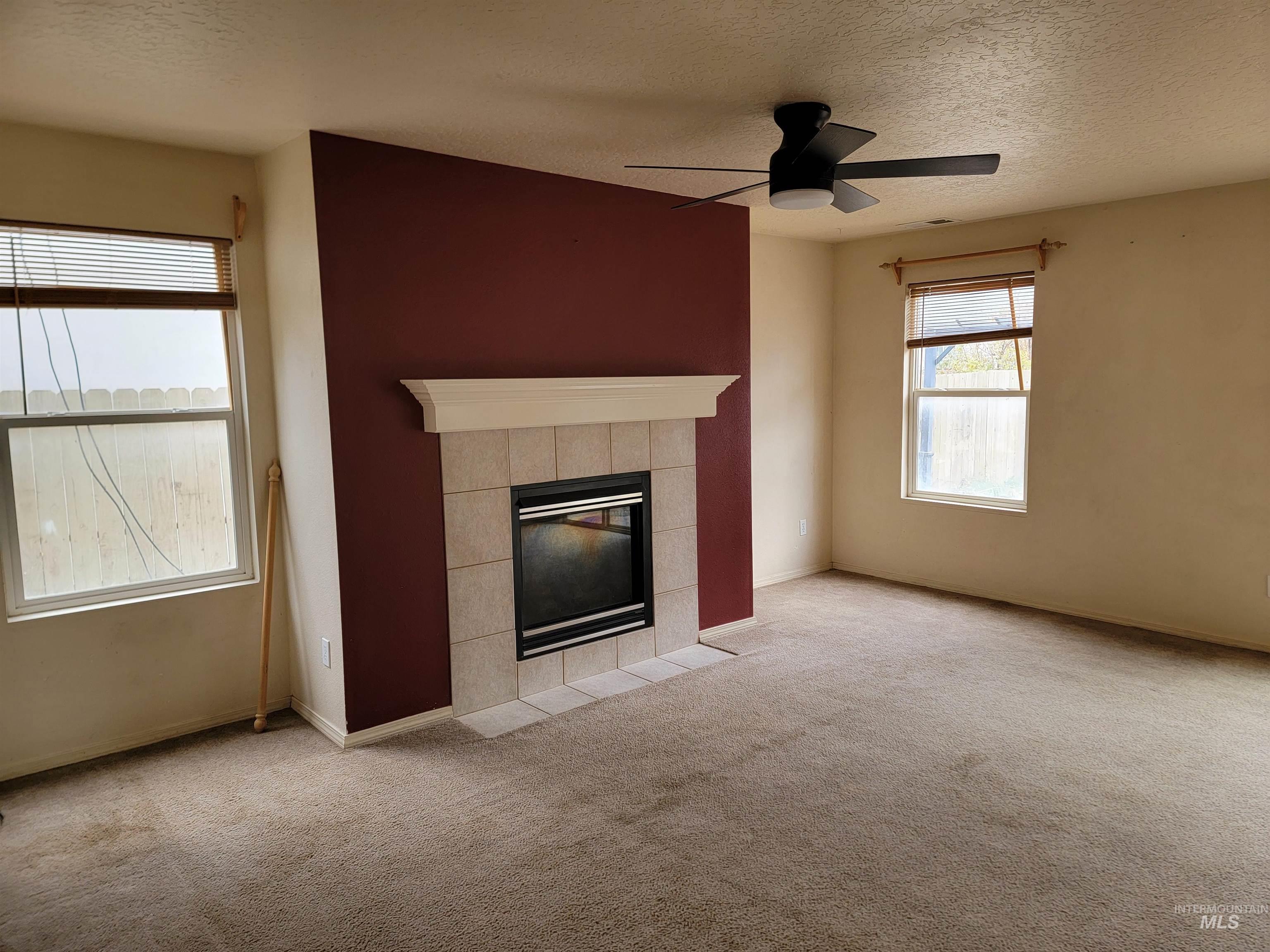 Unfurnished living room with carpet flooring, a tile fireplace, a textured ceiling, and a ceiling fan
