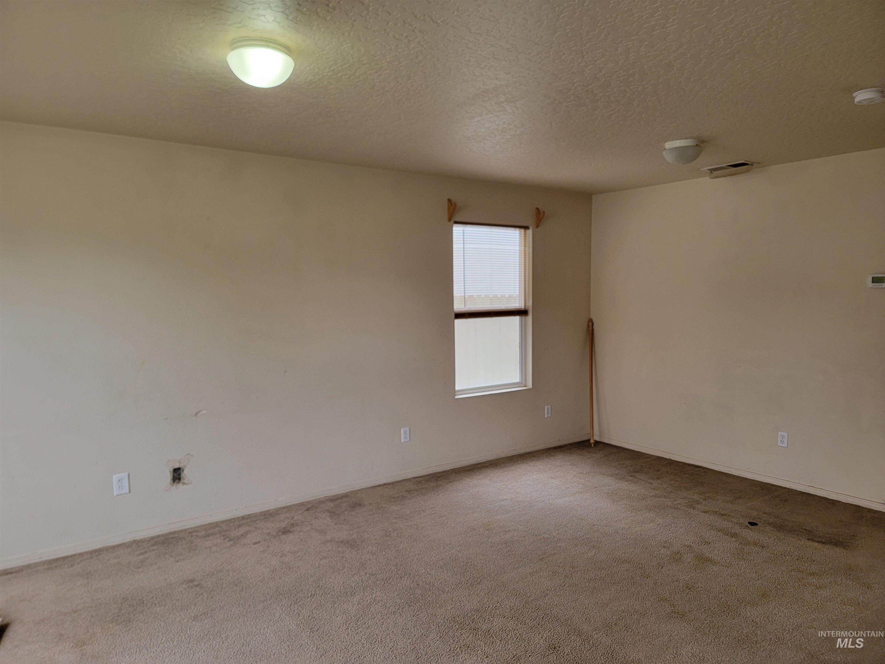 Empty room with light colored carpet, a textured ceiling, and a smoke detector