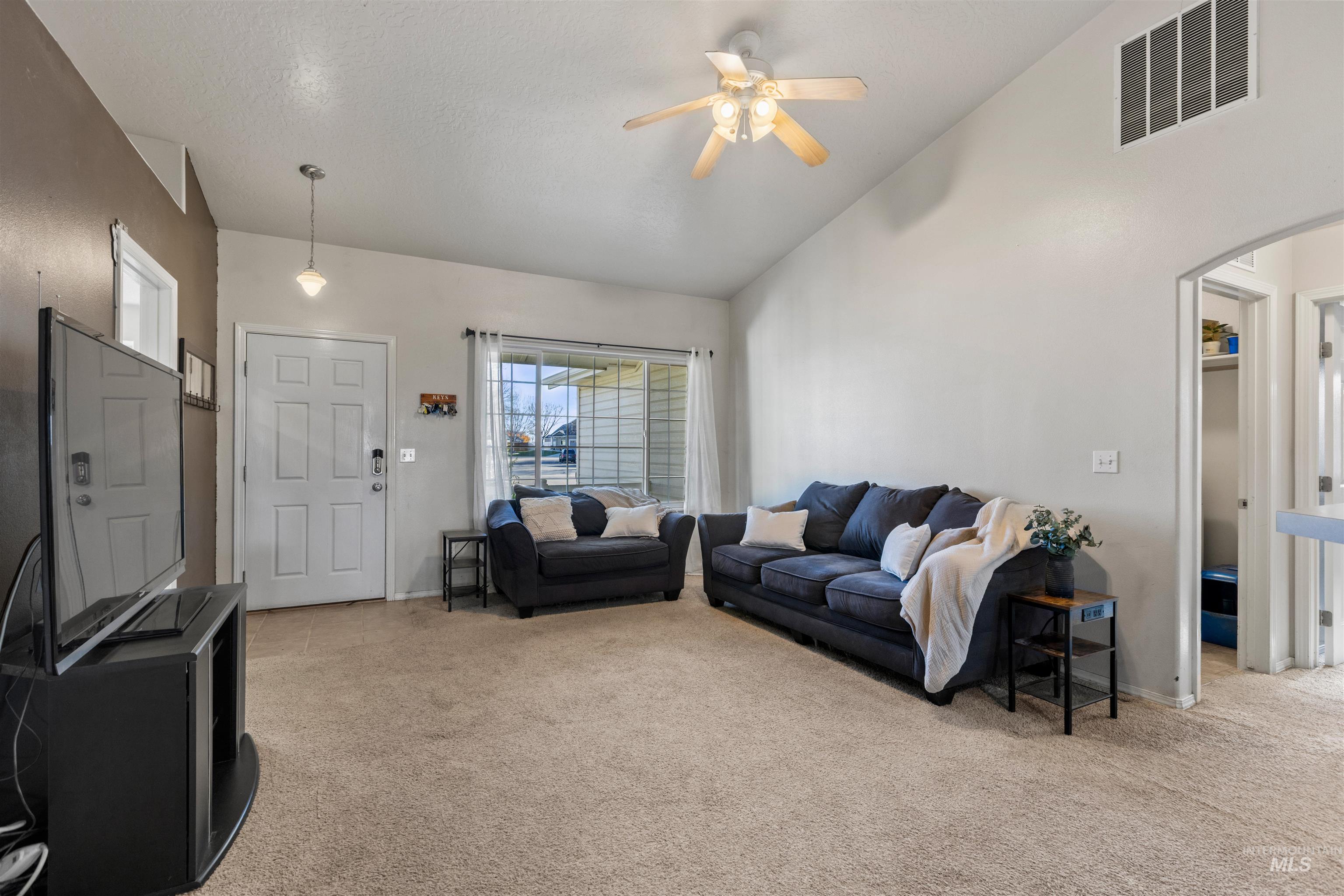 Living room with light carpet, ceiling fan, high vaulted ceiling, and arched walkways