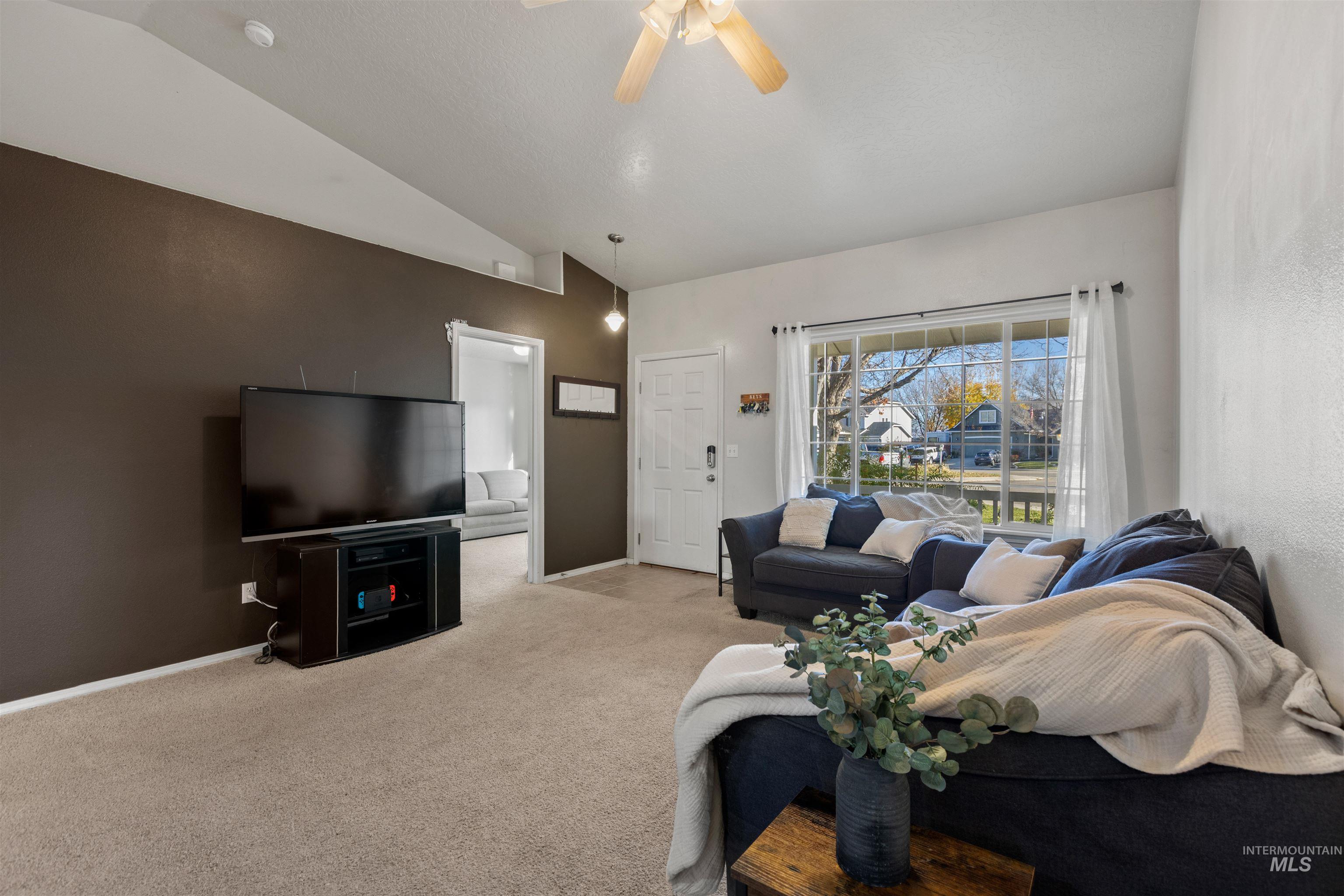Living area featuring vaulted ceiling, light colored carpet, and ceiling fan