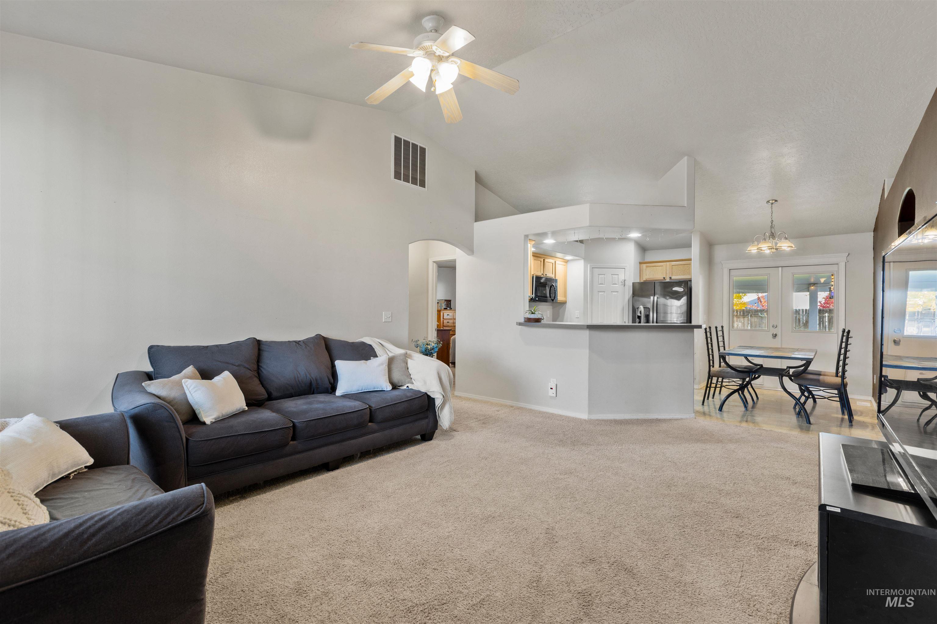 Living room featuring lofted ceiling, light carpet, arched walkways, a chandelier, and a ceiling fan
