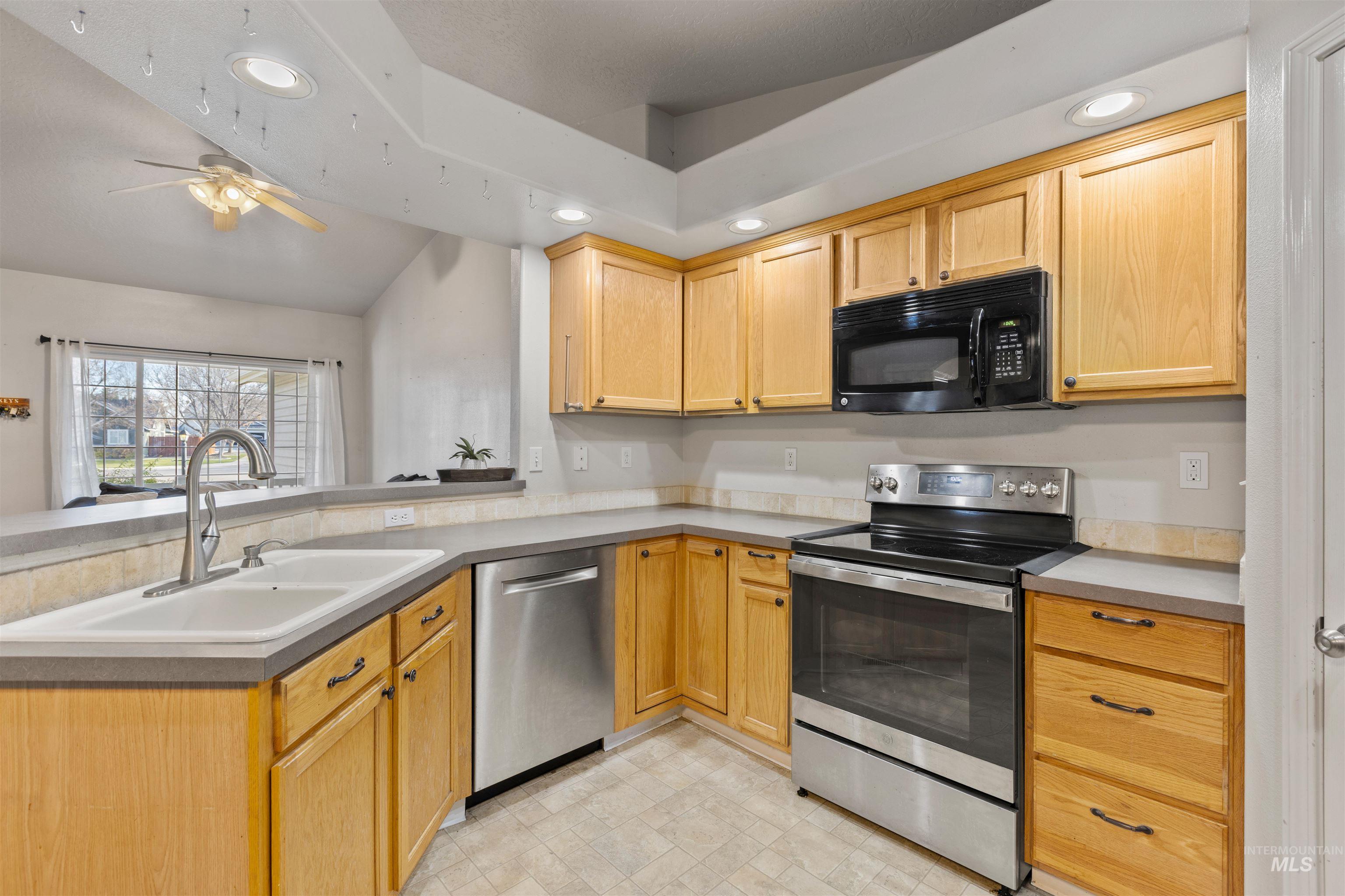 Kitchen featuring recessed lighting, stainless steel appliances, a peninsula, lofted ceiling, and light brown cabinetry