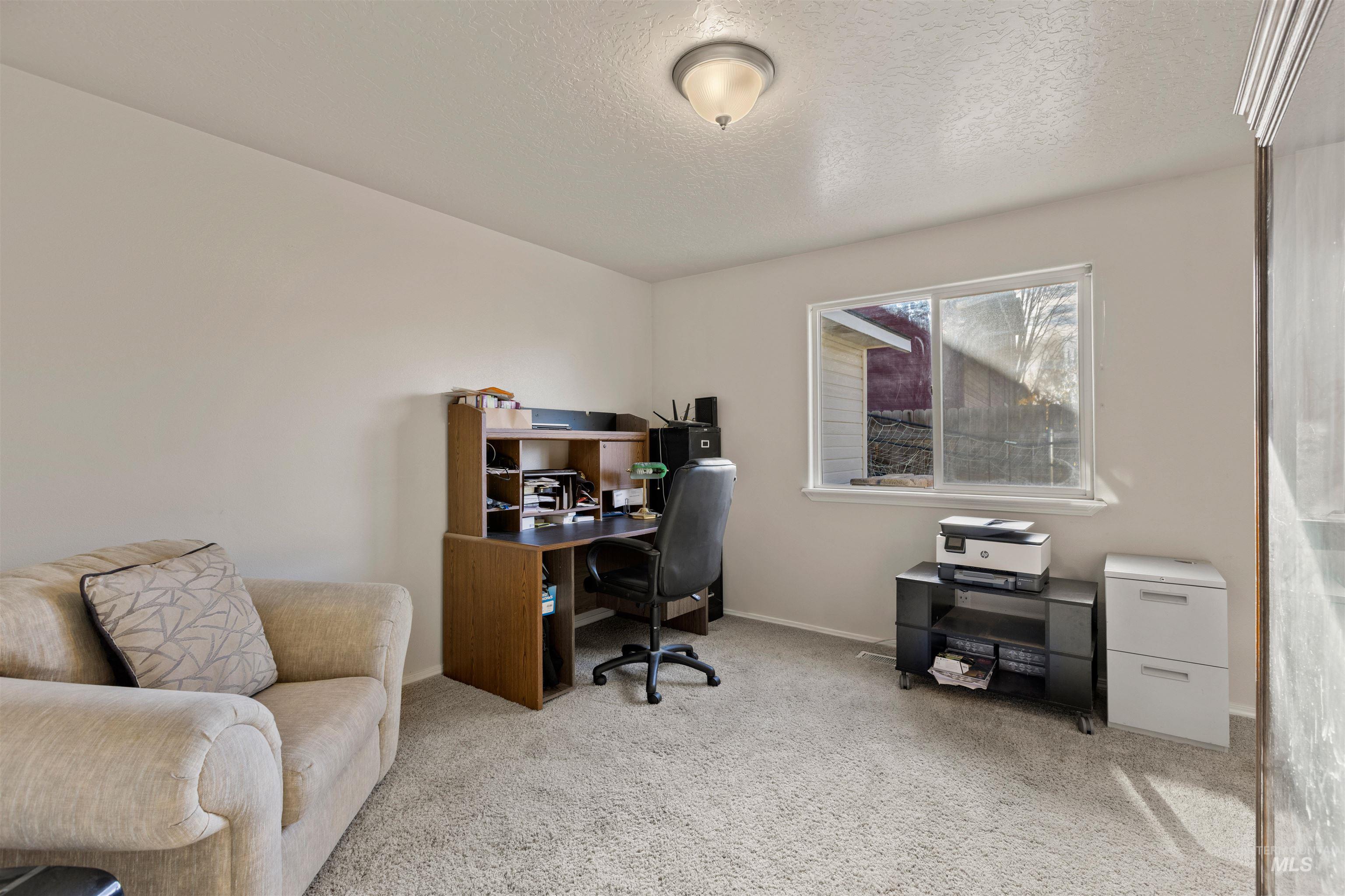 Carpeted home office featuring a textured ceiling and baseboards