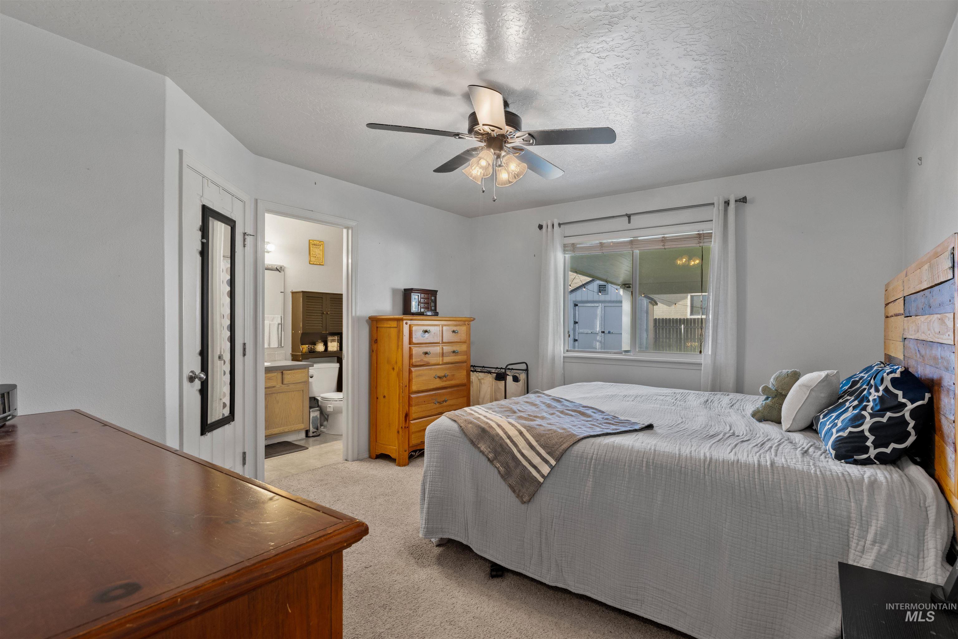 Bedroom with light colored carpet, a textured ceiling, a ceiling fan, and connected bathroom