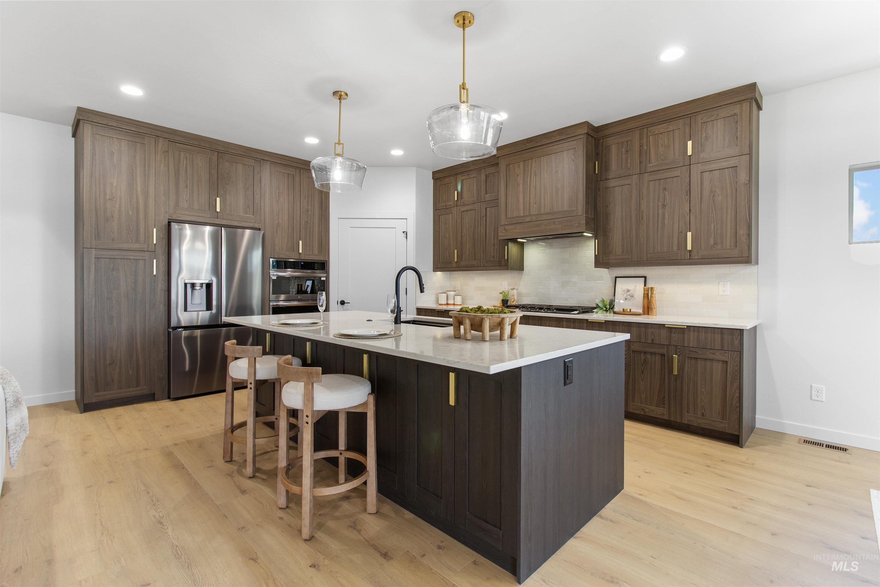 Kitchen with tasteful backsplash, appliances with stainless steel finishes, a kitchen bar, hanging light fixtures, and an island with sink