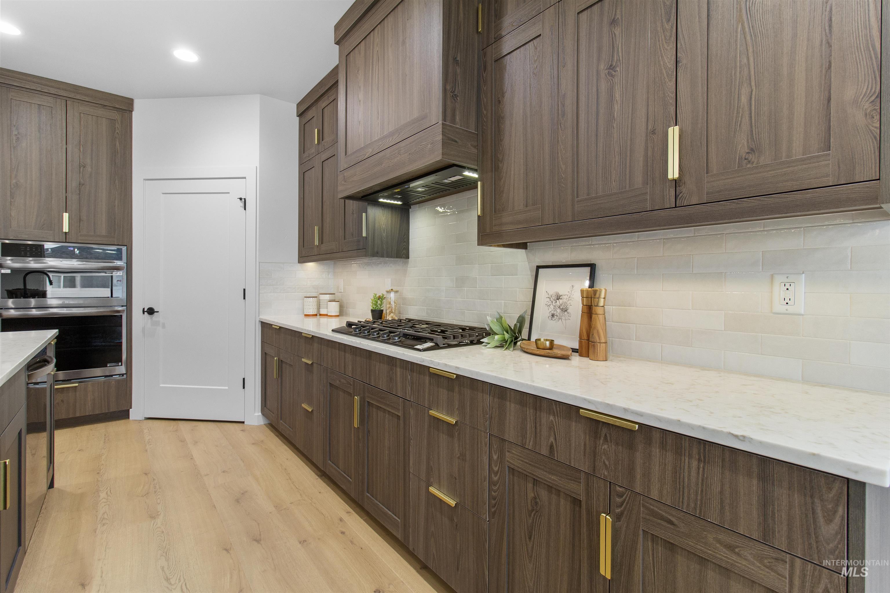Kitchen with light wood-style floors, backsplash, light stone counters, double oven, and black gas cooktop