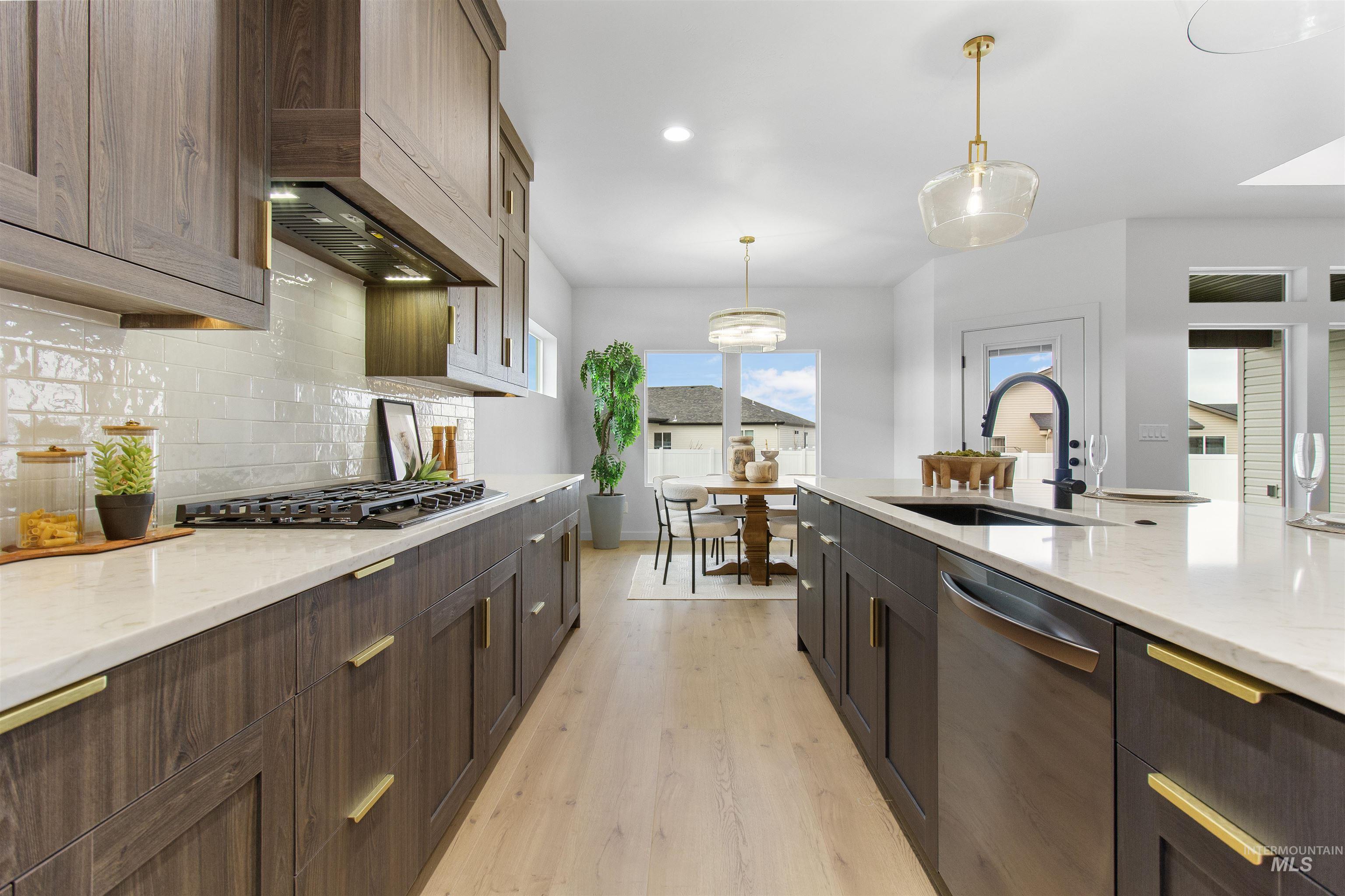 Kitchen featuring light stone counters, decorative light fixtures, light wood-style flooring, stainless steel dishwasher, and recessed lighting