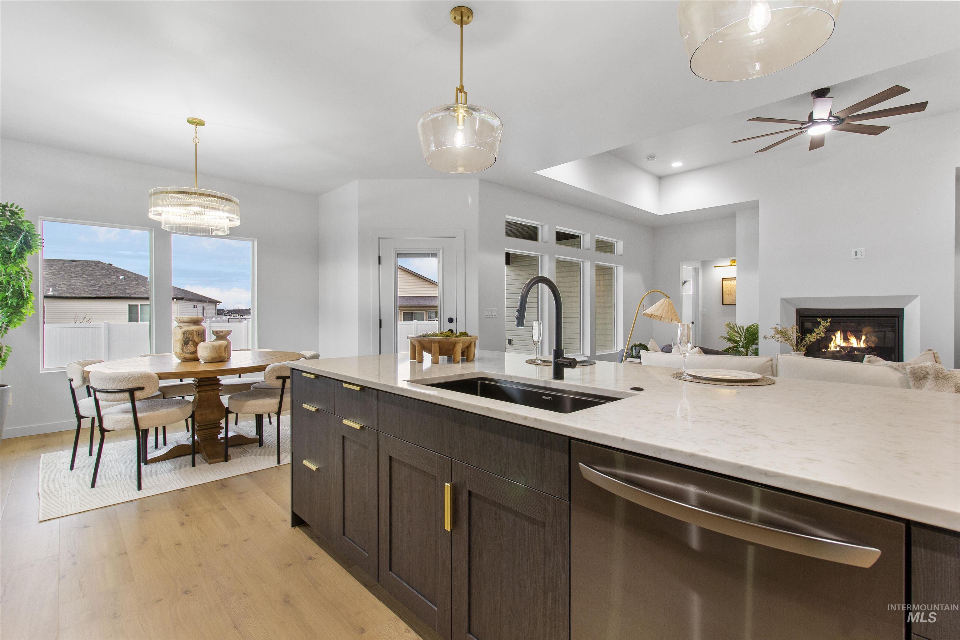 Kitchen with stainless steel dishwasher, hanging light fixtures, light wood-style floors, dark brown cabinets, and recessed lighting