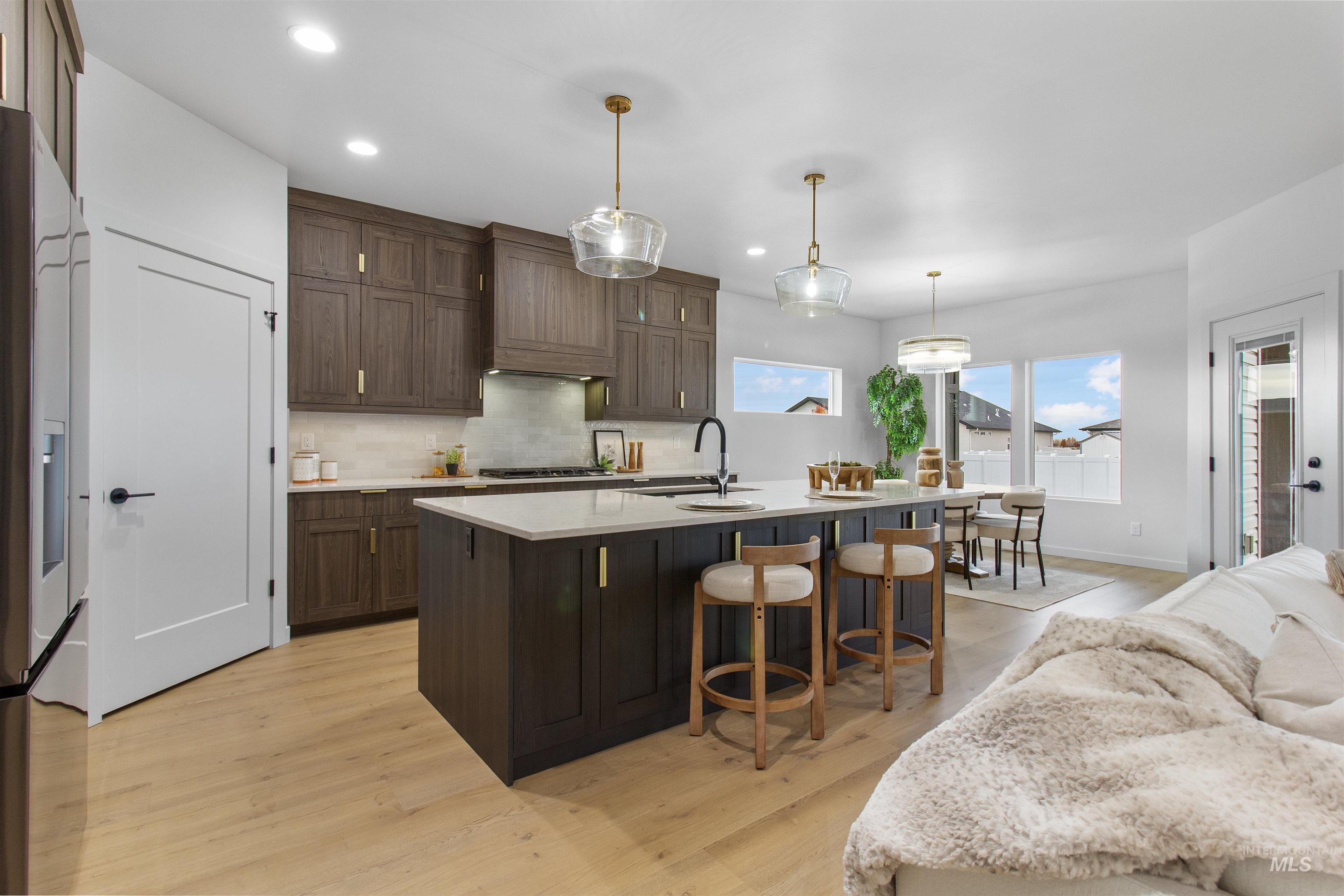 Kitchen featuring backsplash, stainless steel refrigerator with ice dispenser, dark brown cabinets, hanging light fixtures, and a breakfast bar