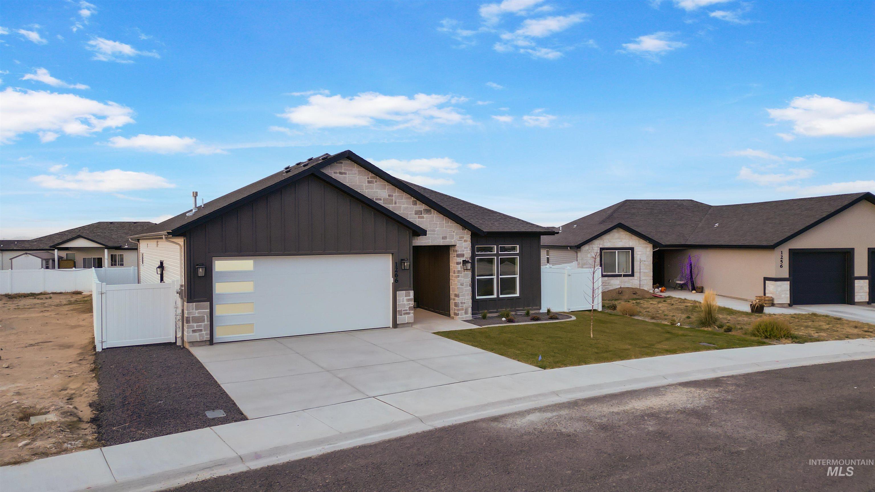 View of front of property featuring stone siding, board and batten siding, a garage, concrete driveway, and a gate