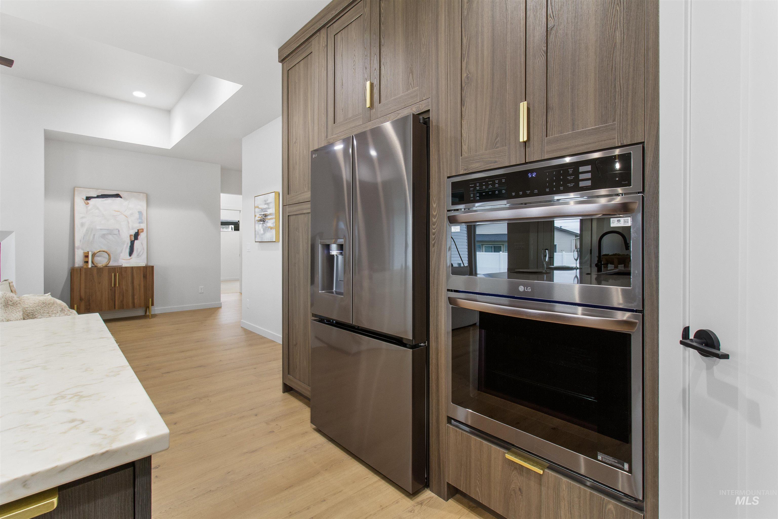 Kitchen with appliances with stainless steel finishes, light wood finished floors, recessed lighting, and brown cabinets