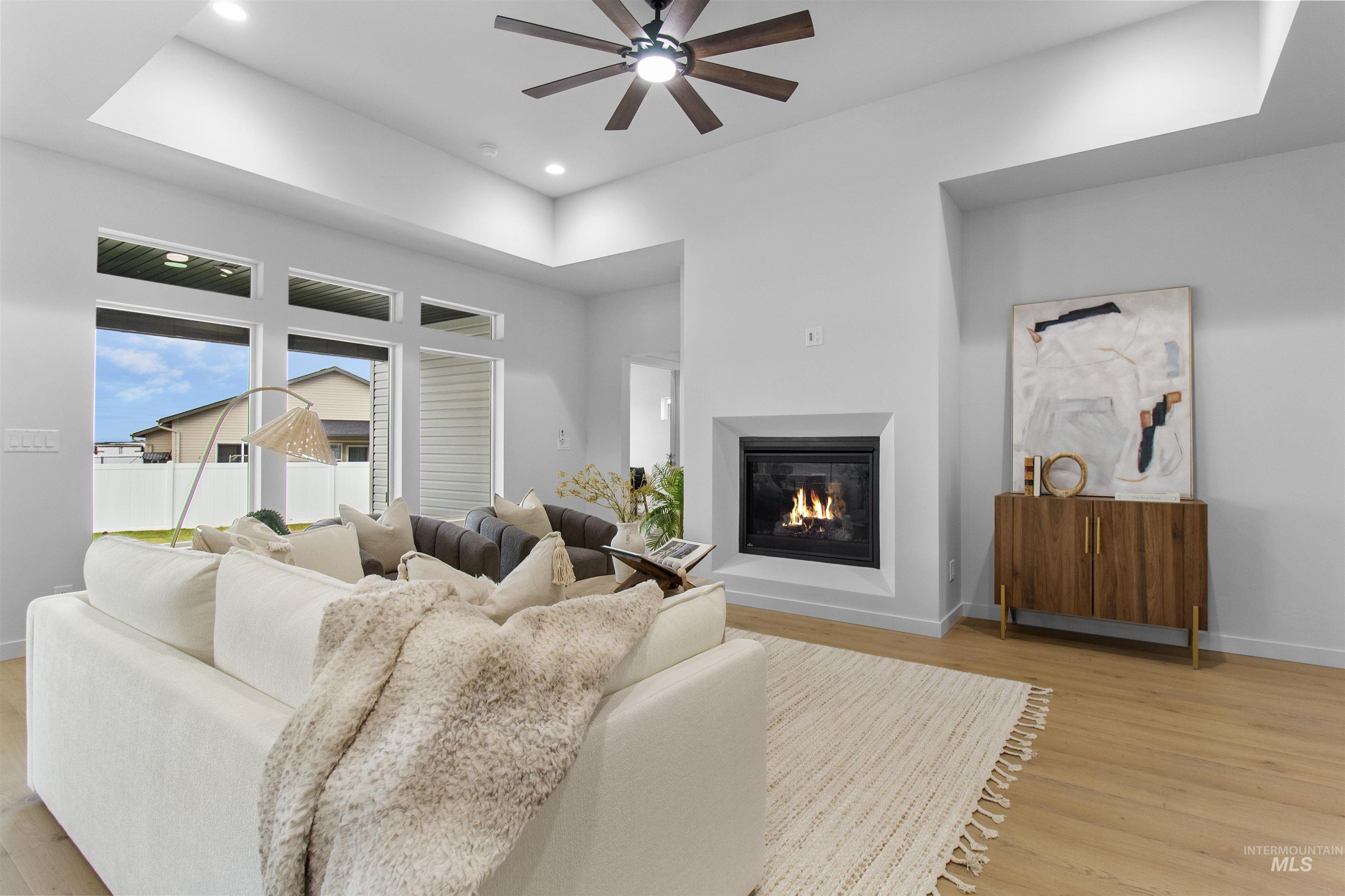 Living area with a glass covered fireplace, light wood-style flooring, recessed lighting, a ceiling fan, and a tray ceiling