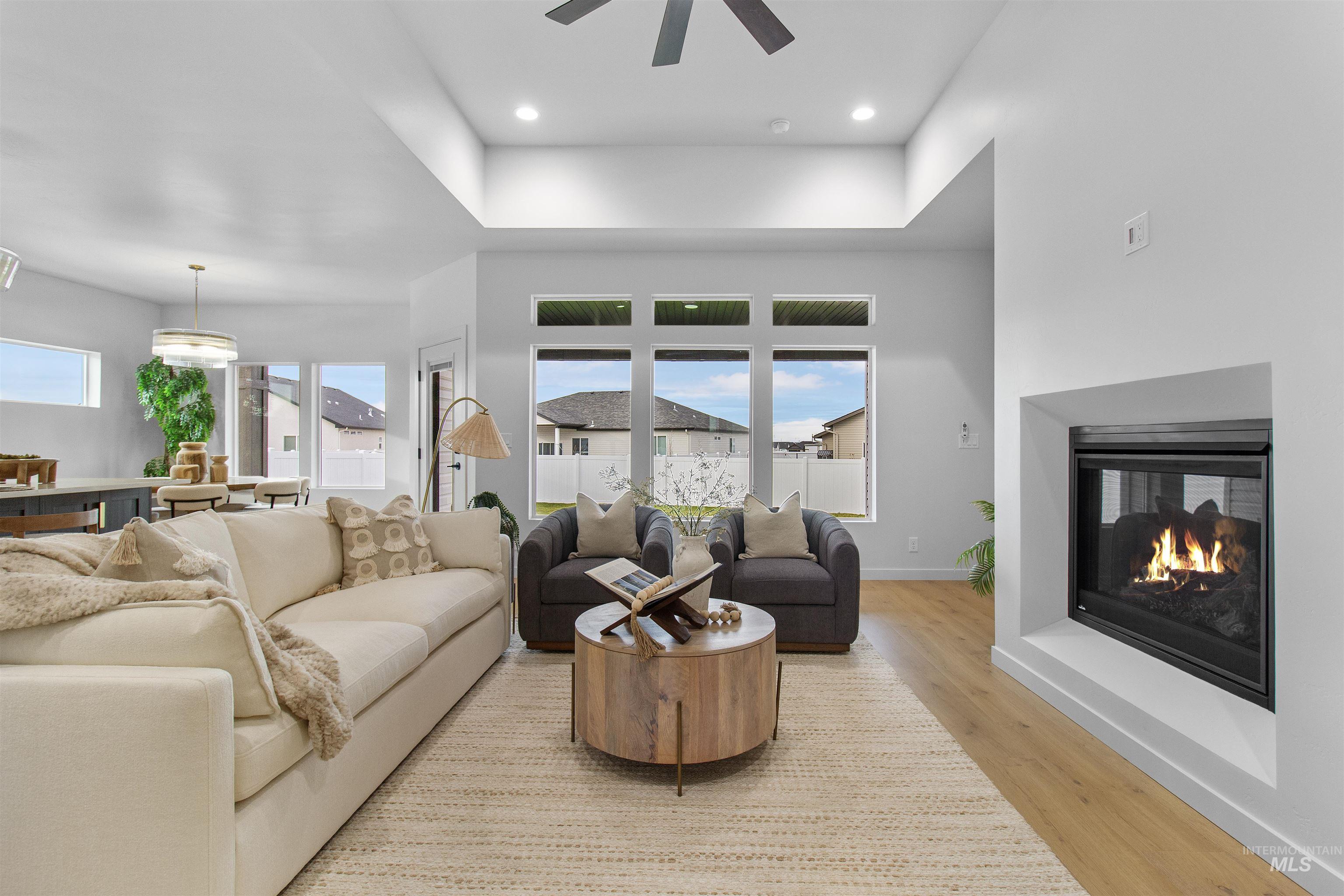 Living area with light wood-style flooring, a multi sided fireplace, recessed lighting, and a raised ceiling