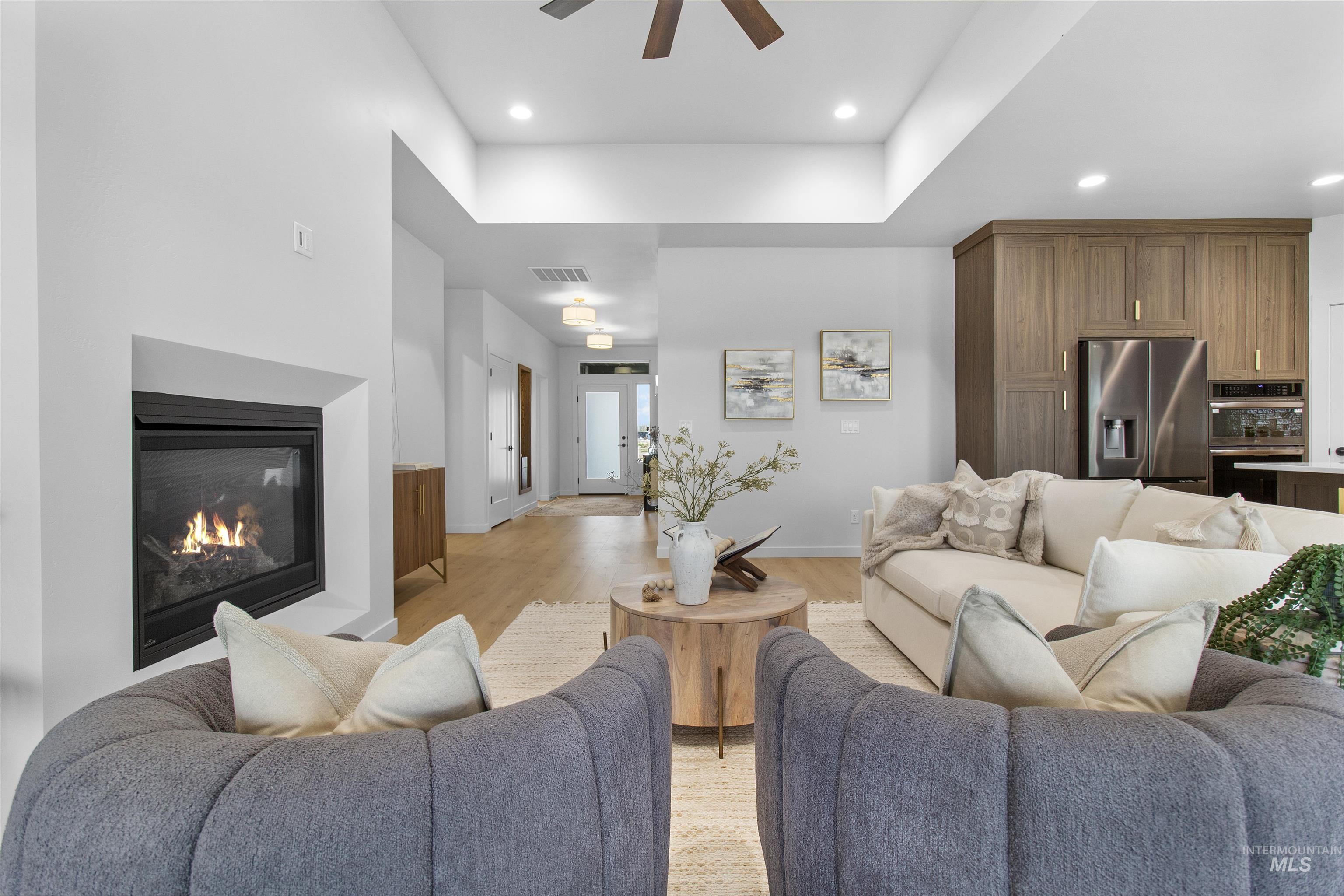 Living room featuring a glass covered fireplace, light wood-style floors, recessed lighting, a ceiling fan, and a raised ceiling