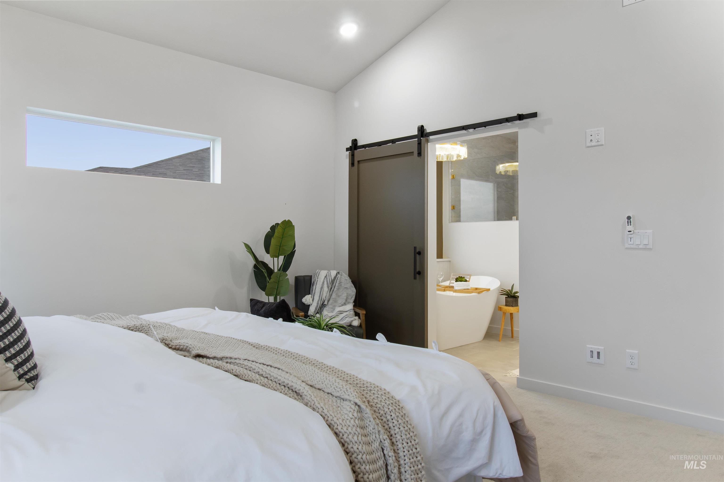 Bedroom with a barn door, light colored carpet, ensuite bathroom, and recessed lighting