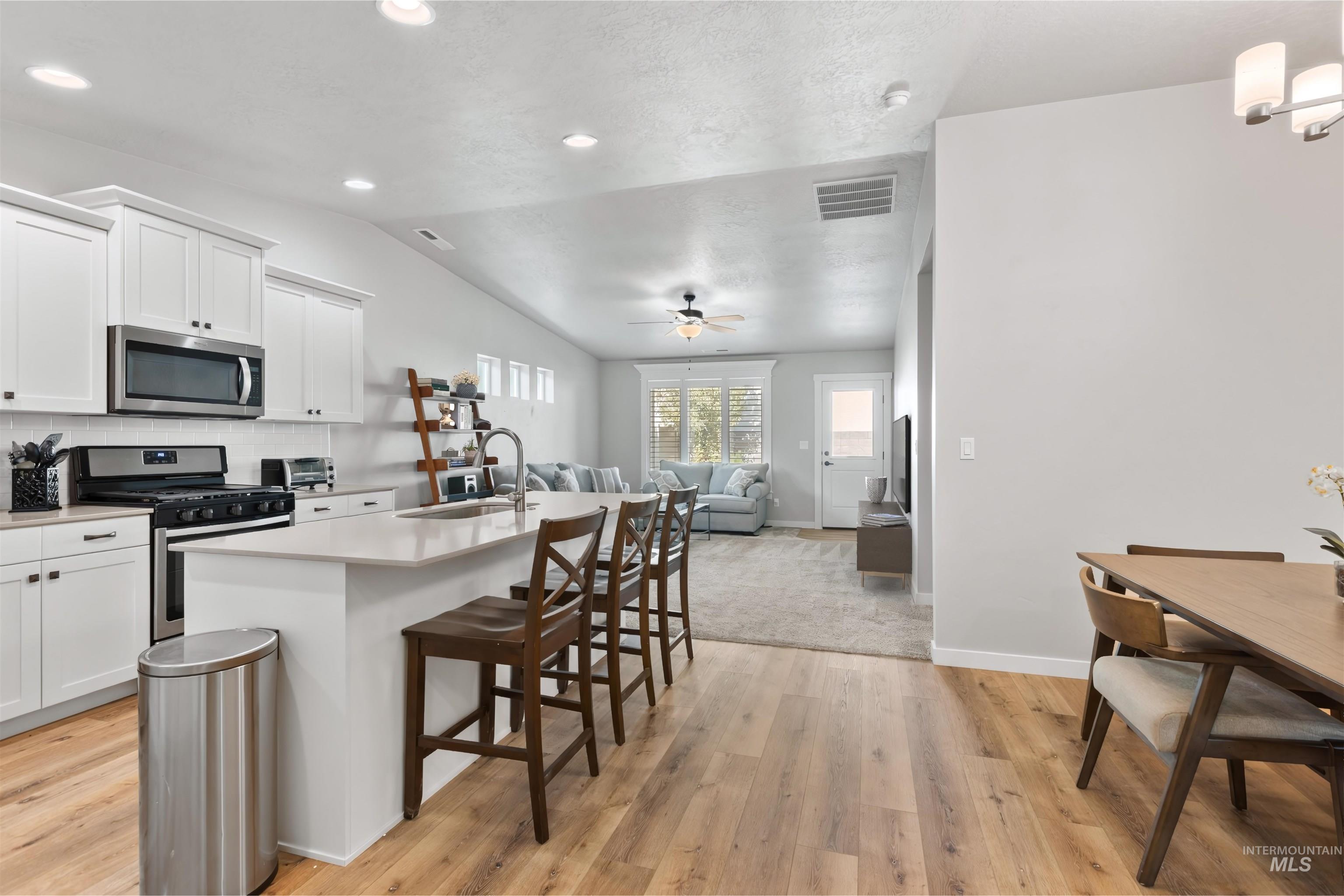 Kitchen featuring stainless steel appliances, a center island with sink, tasteful backsplash, a breakfast bar, and white cabinetry