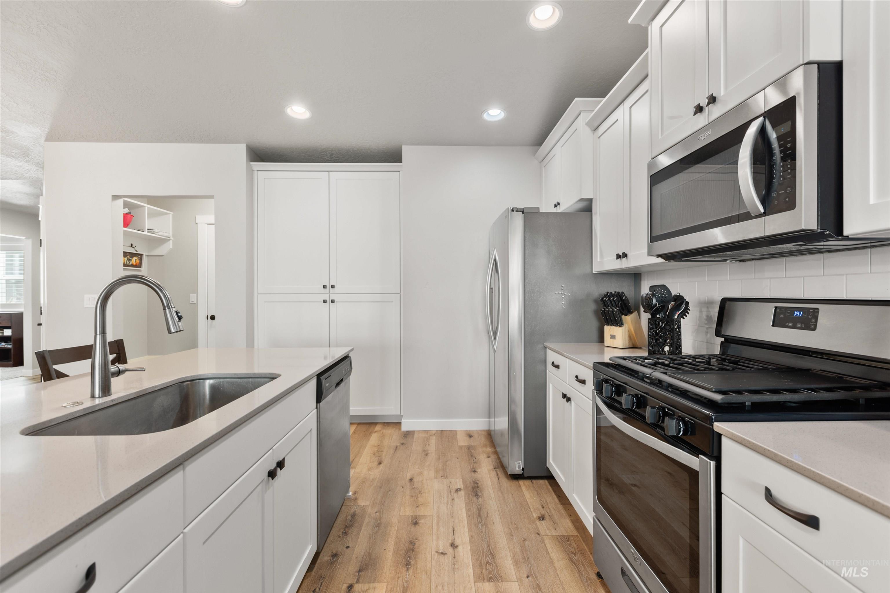 Kitchen featuring appliances with stainless steel finishes, white cabinetry, light wood-type flooring, recessed lighting, and light stone counters