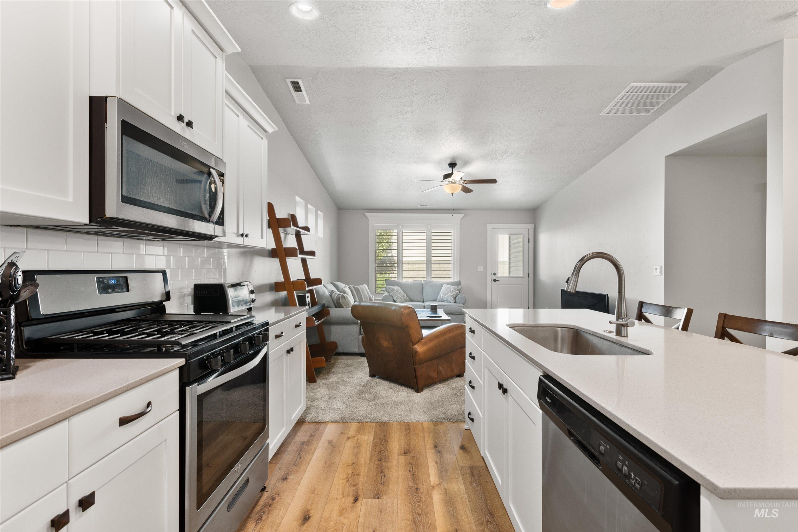 Kitchen featuring stainless steel appliances, white cabinets, light wood finished floors, backsplash, and open floor plan