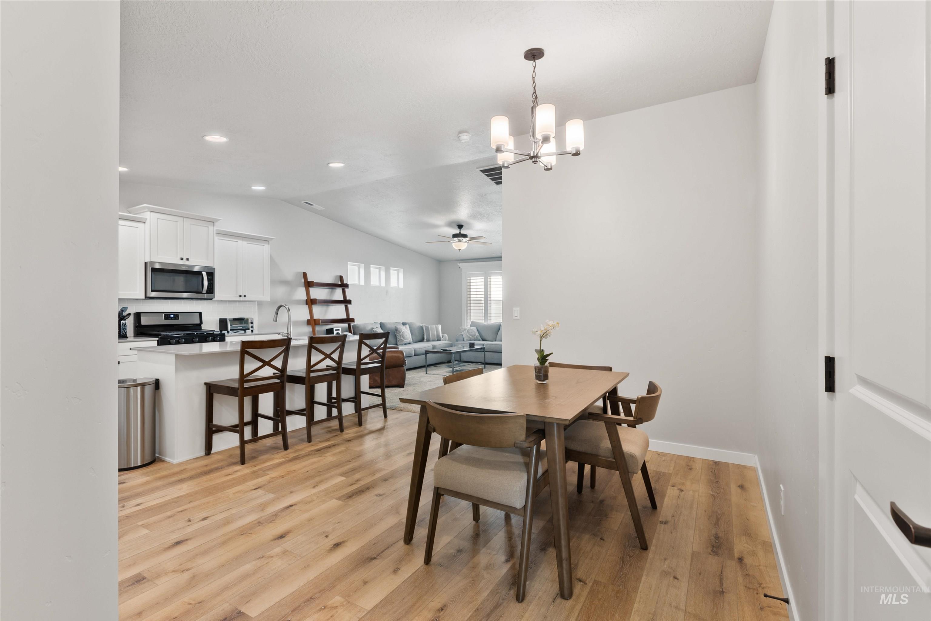 Dining area featuring light wood-style flooring, a chandelier, ceiling fan, vaulted ceiling, and recessed lighting