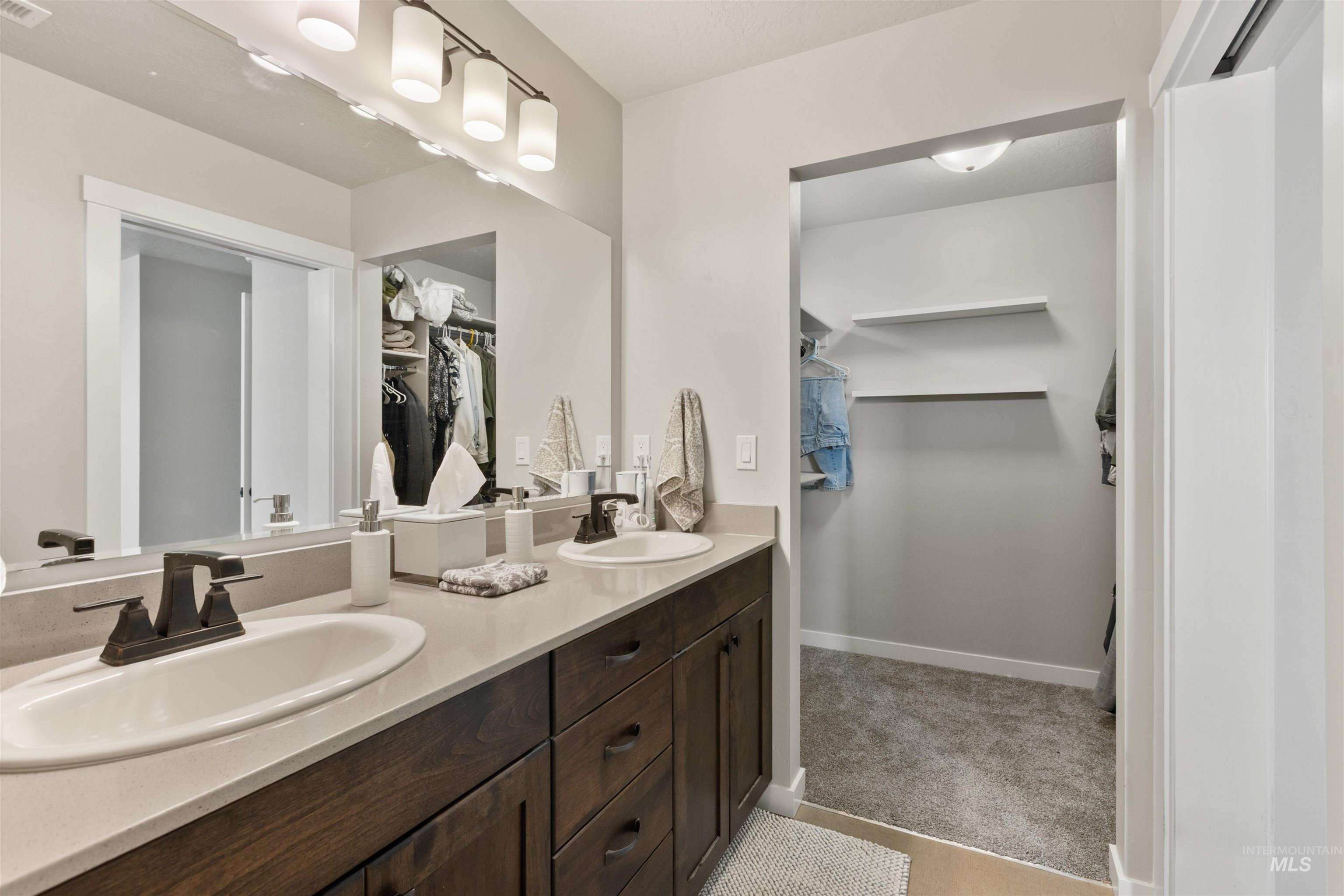 Full bath with a walk in closet, double vanity, and light carpet