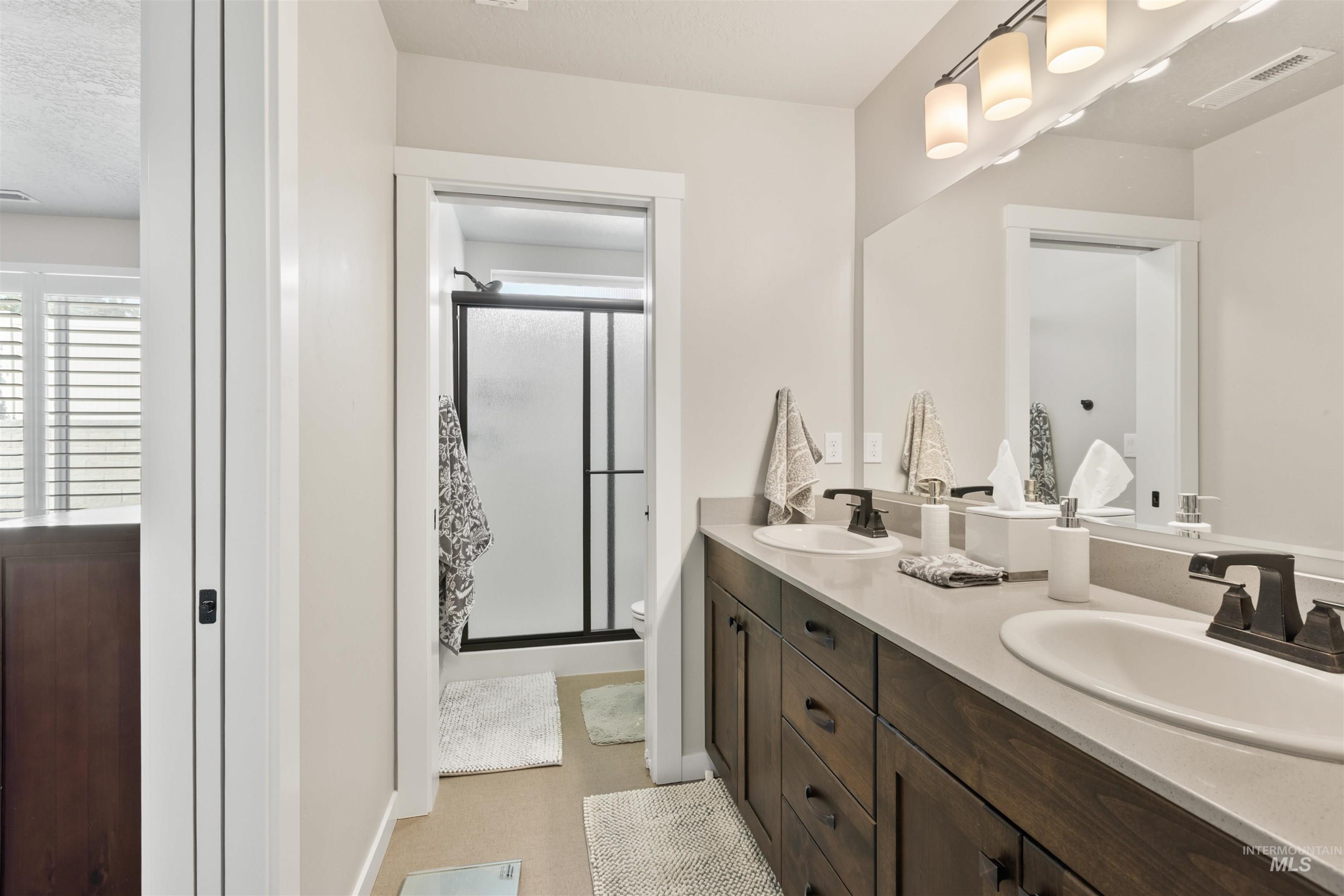 Full bathroom featuring double vanity, a stall shower, healthy amount of natural light, and a textured ceiling