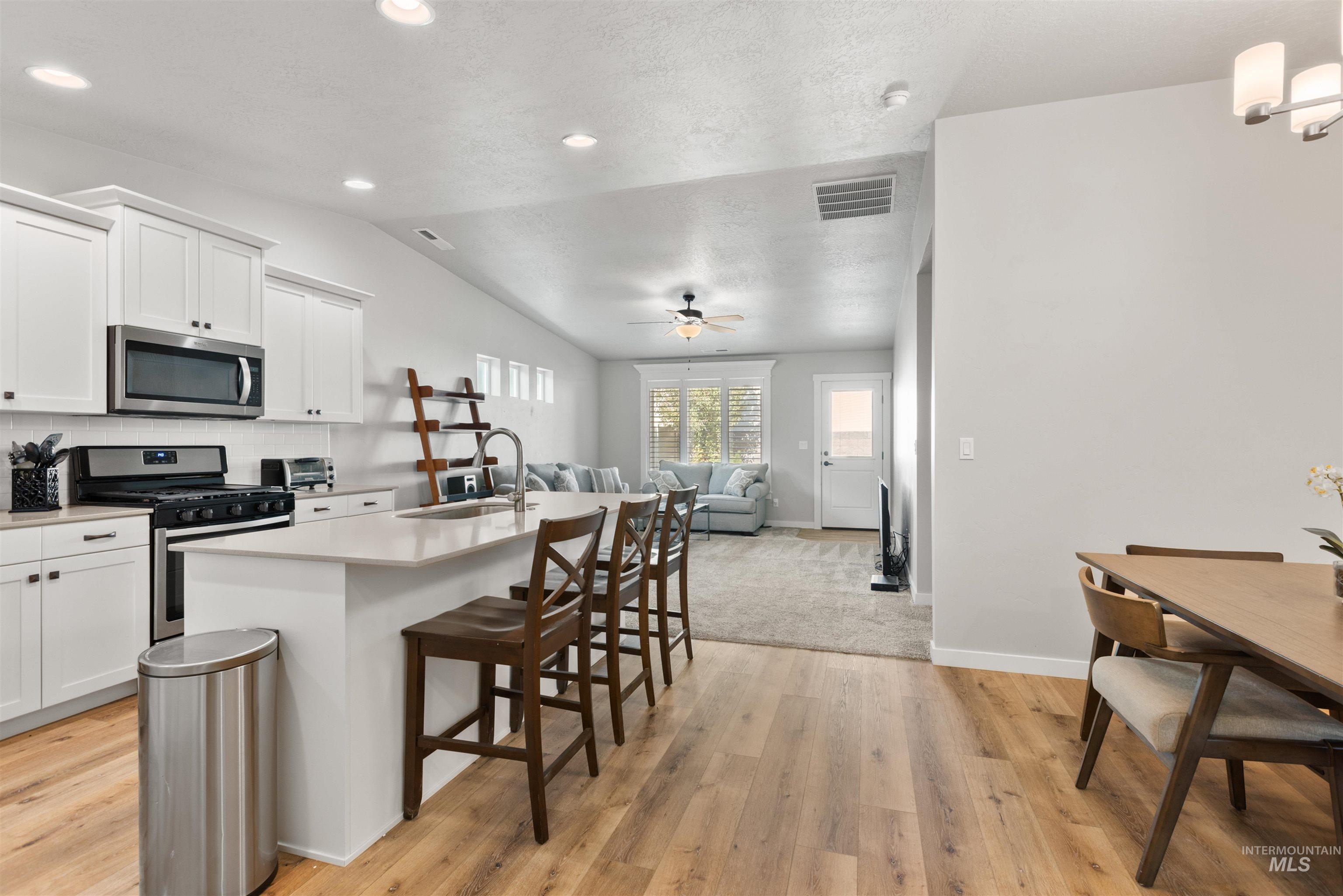 Kitchen with a breakfast bar, a center island with sink, stainless steel appliances, decorative backsplash, and white cabinetry