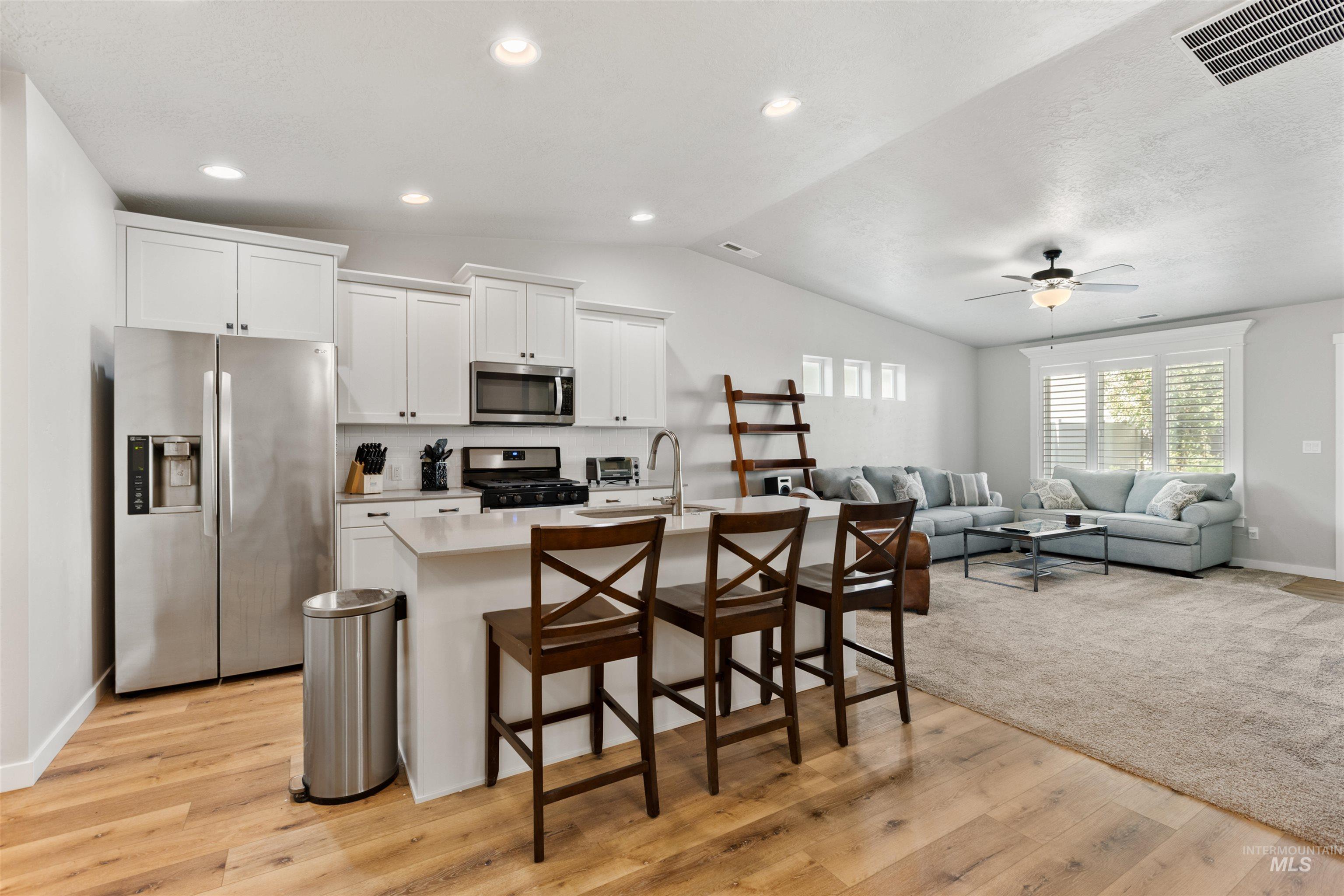 Kitchen featuring stainless steel appliances, white cabinetry, vaulted ceiling, a breakfast bar area, and light wood-style flooring