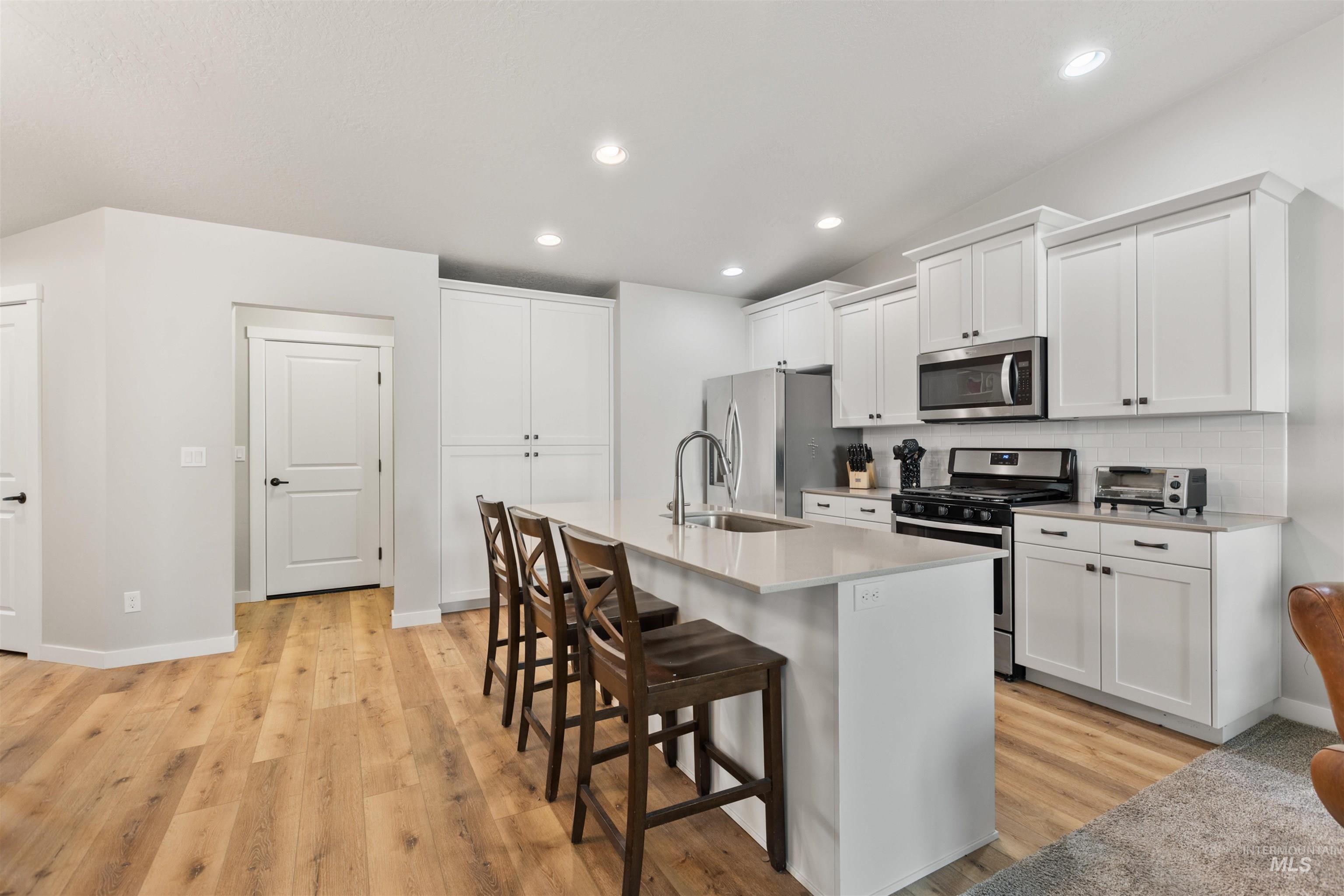 Kitchen featuring stainless steel appliances, a kitchen bar, white cabinets, a center island with sink, and recessed lighting