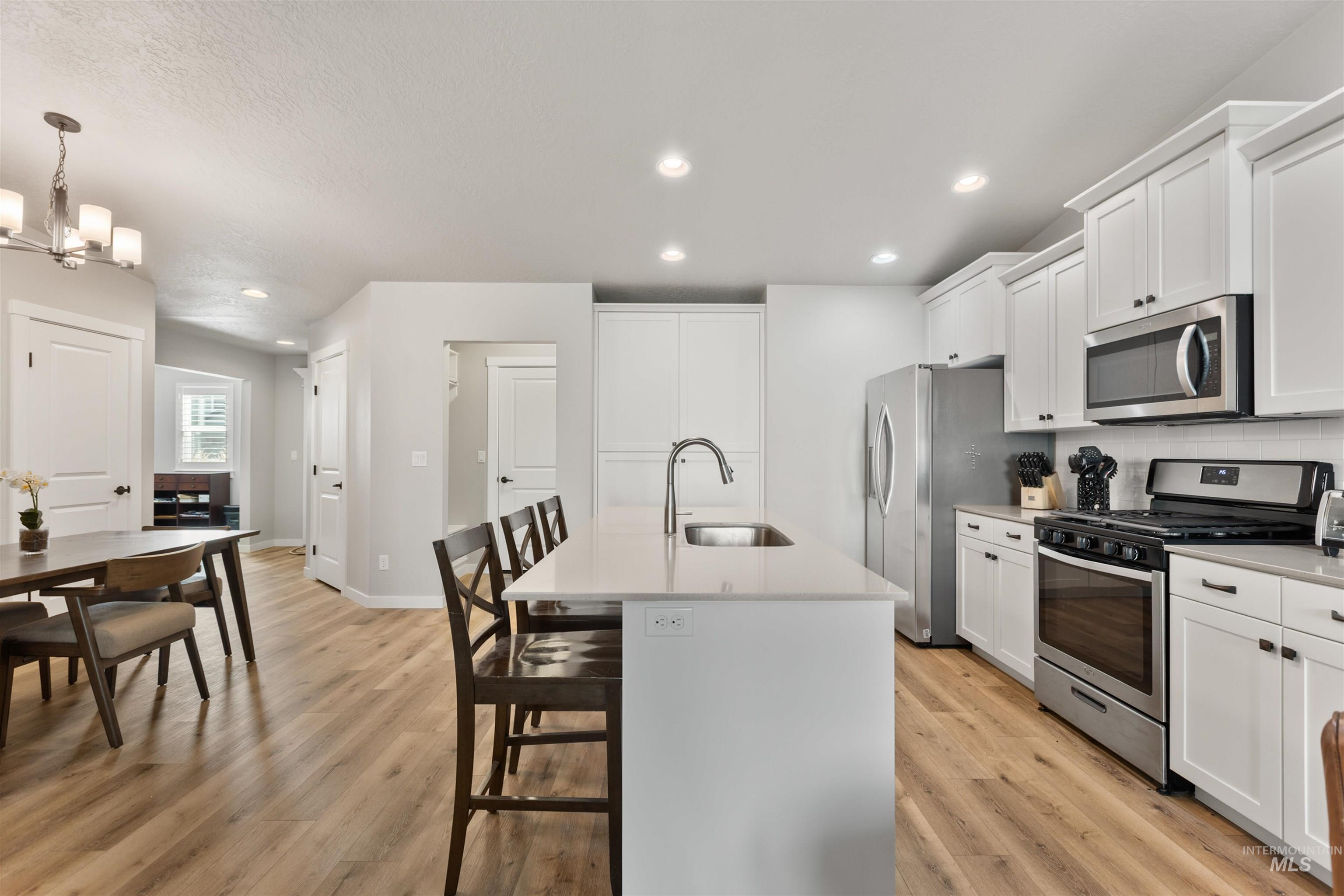 Kitchen with appliances with stainless steel finishes, a breakfast bar, a center island with sink, white cabinets, and recessed lighting