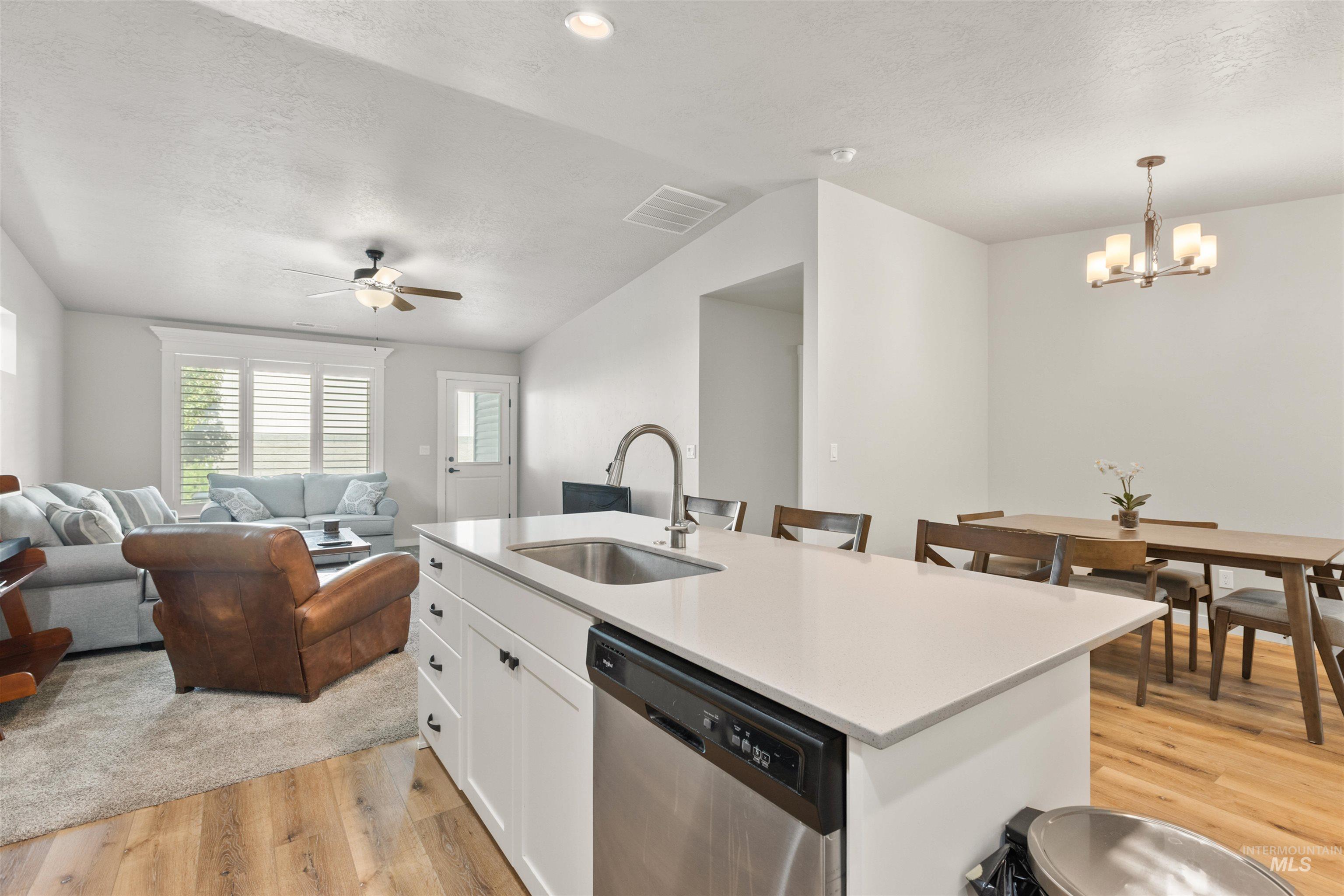 Kitchen featuring stainless steel dishwasher, a textured ceiling, open floor plan, light wood finished floors, and white cabinetry