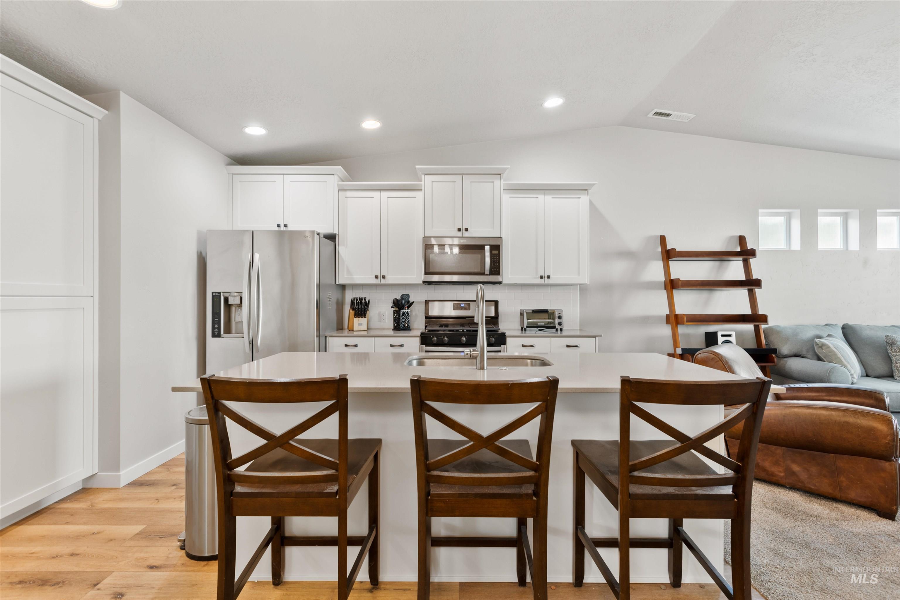 Kitchen with appliances with stainless steel finishes, white cabinetry, vaulted ceiling, open floor plan, and an island with sink