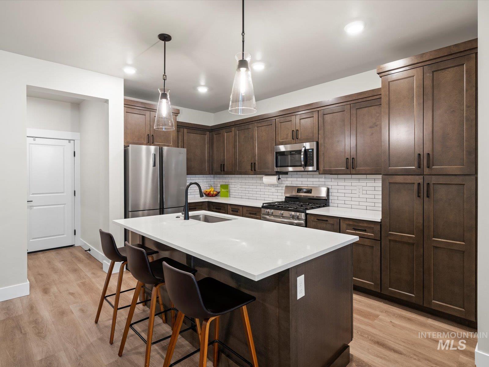 Kitchen with dark brown cabinets, stainless steel appliances, a center island with sink, decorative backsplash, and recessed lighting