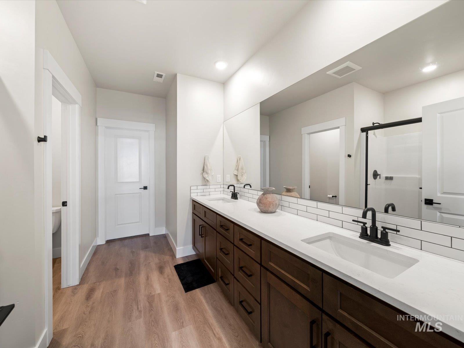 Full bath with double vanity, light wood-type flooring, a shower stall, and recessed lighting