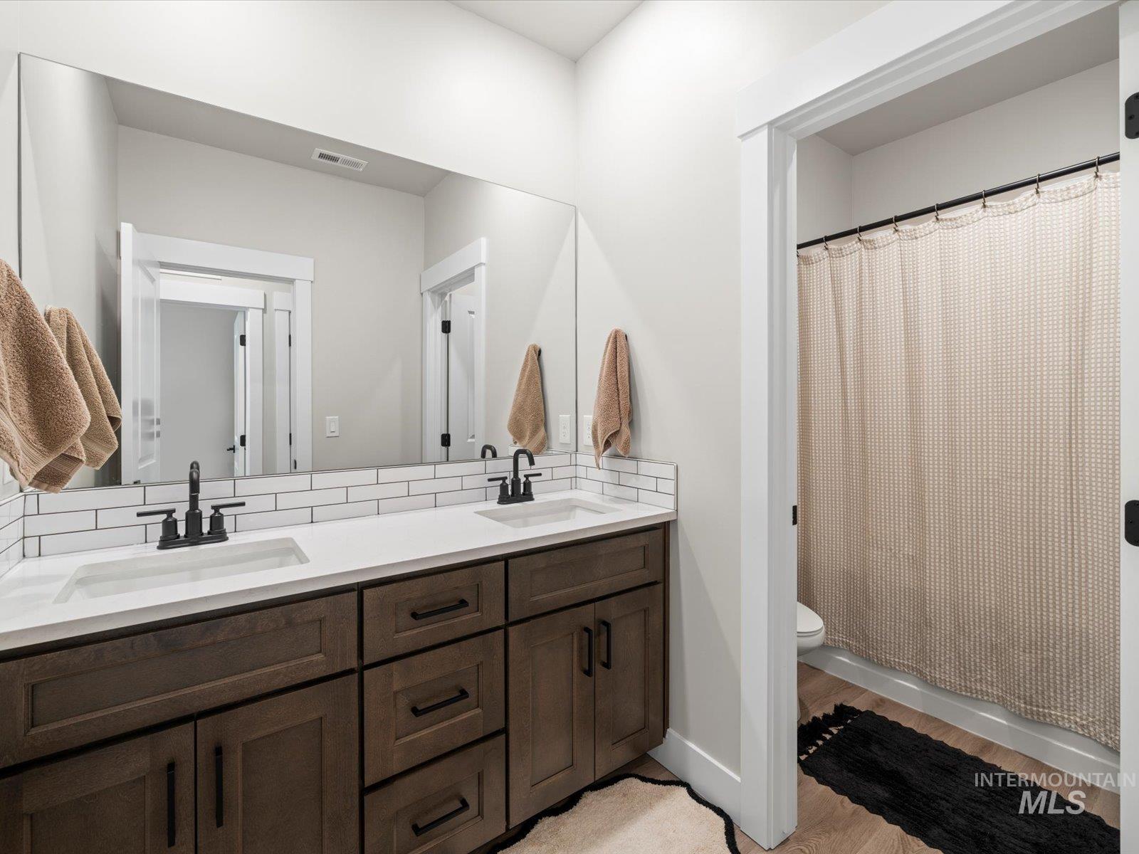 Bathroom featuring double vanity, a shower with curtain, and light wood finished floors