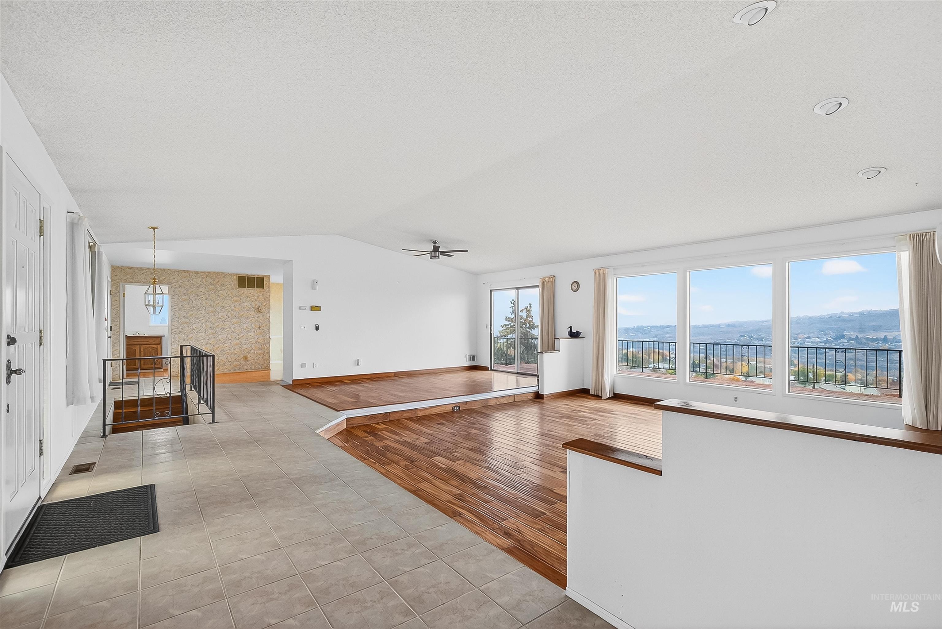Unfurnished living room featuring lofted ceiling, ceiling fan, light tile patterned flooring, and wallpapered walls