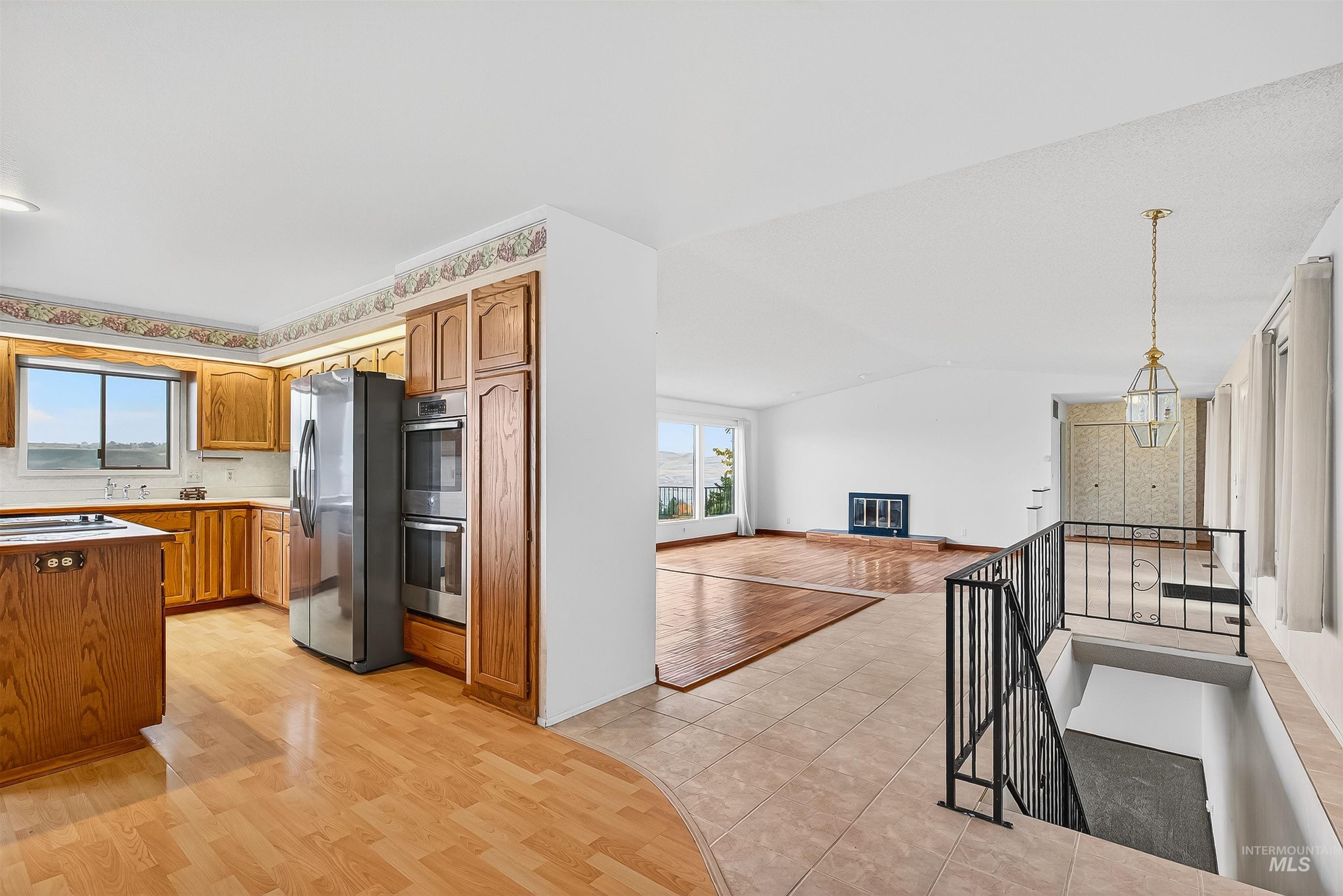 Kitchen featuring light wood finished floors, vaulted ceiling, appliances with stainless steel finishes, brown cabinets, and open floor plan