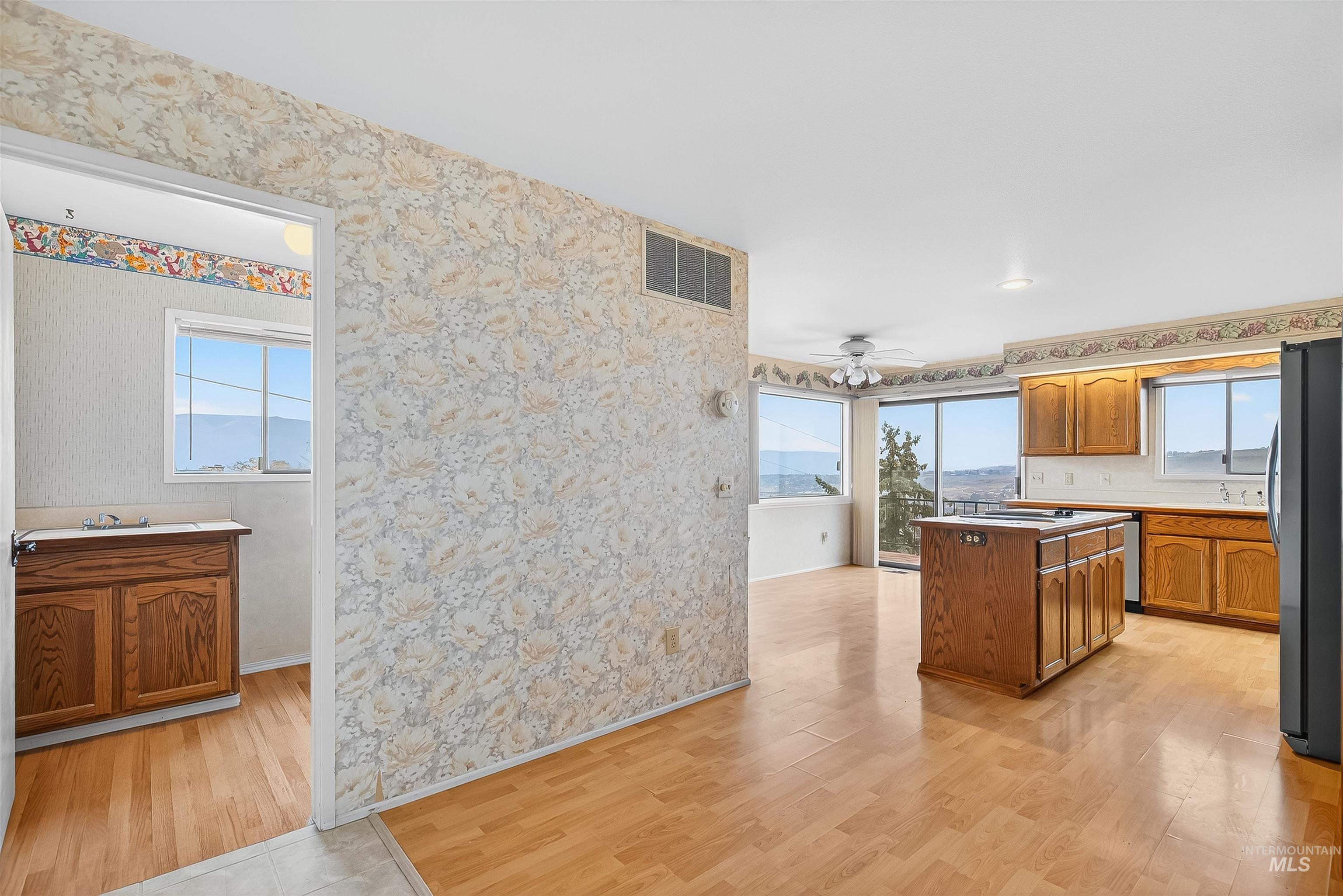 Kitchen with wallpapered walls, brown cabinetry, light wood finished floors, a ceiling fan, and freestanding refrigerator