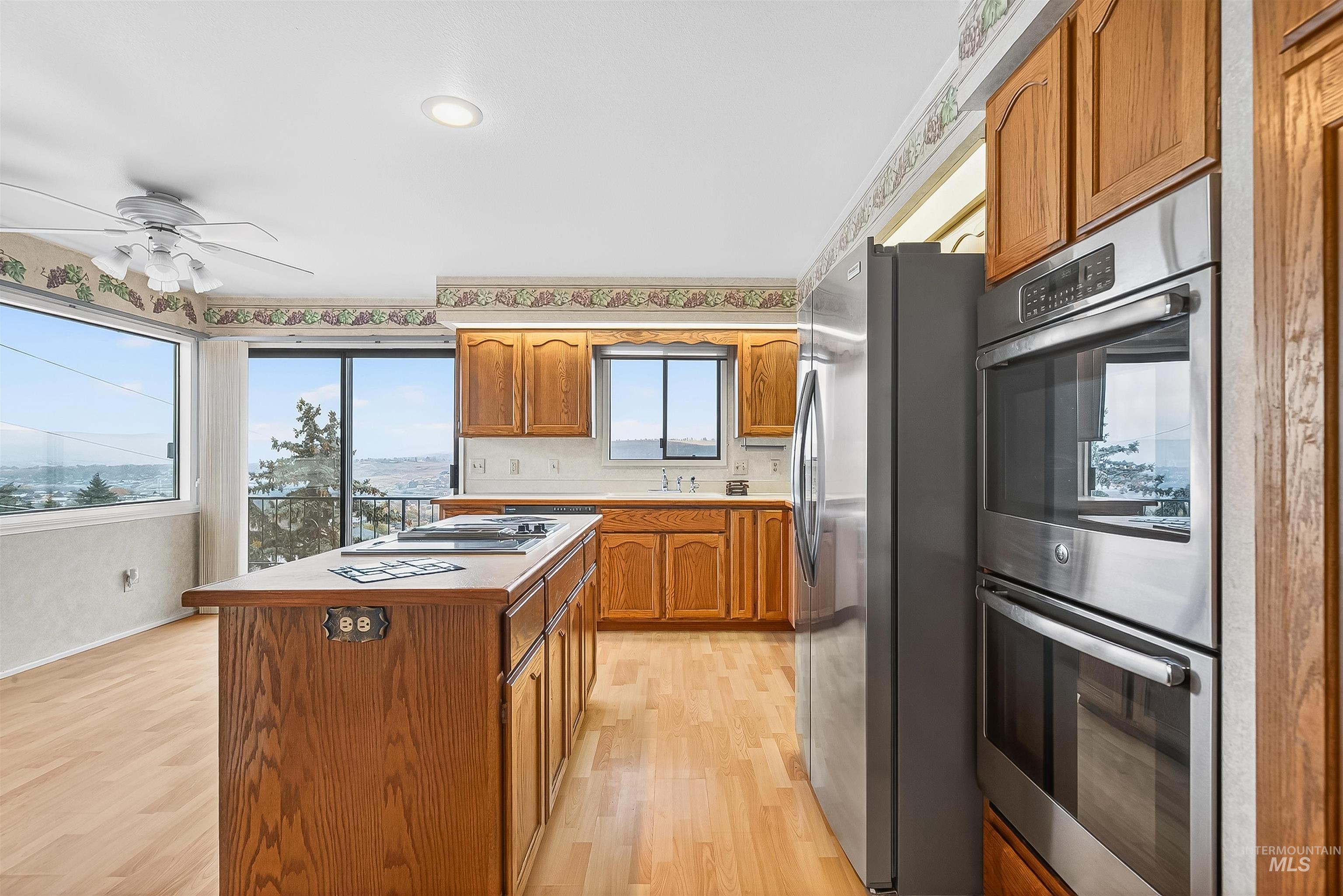 Kitchen featuring appliances with stainless steel finishes, brown cabinets, light wood-type flooring, and light countertops