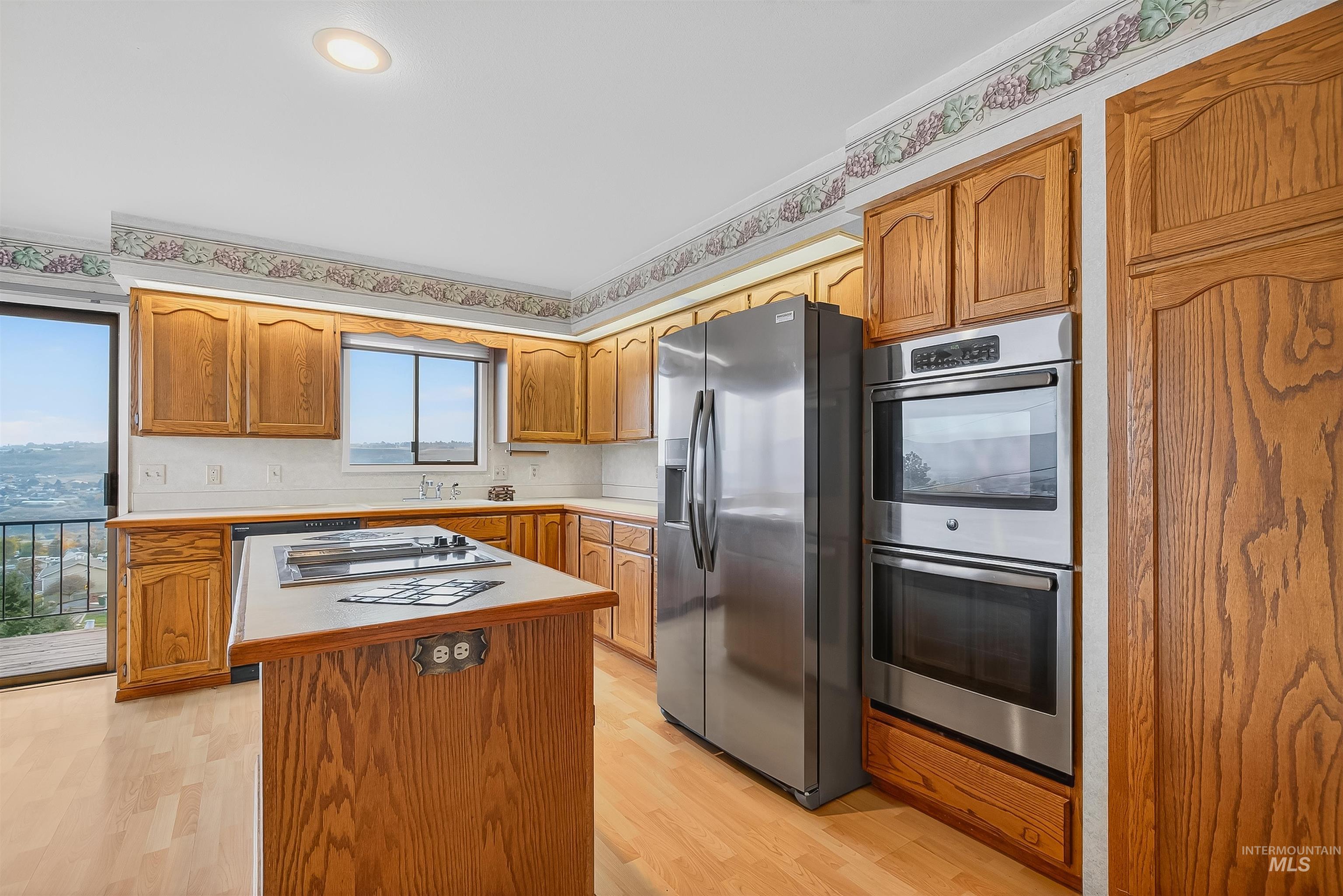 Kitchen featuring brown cabinetry, appliances with stainless steel finishes, light countertops, and light wood-style floors