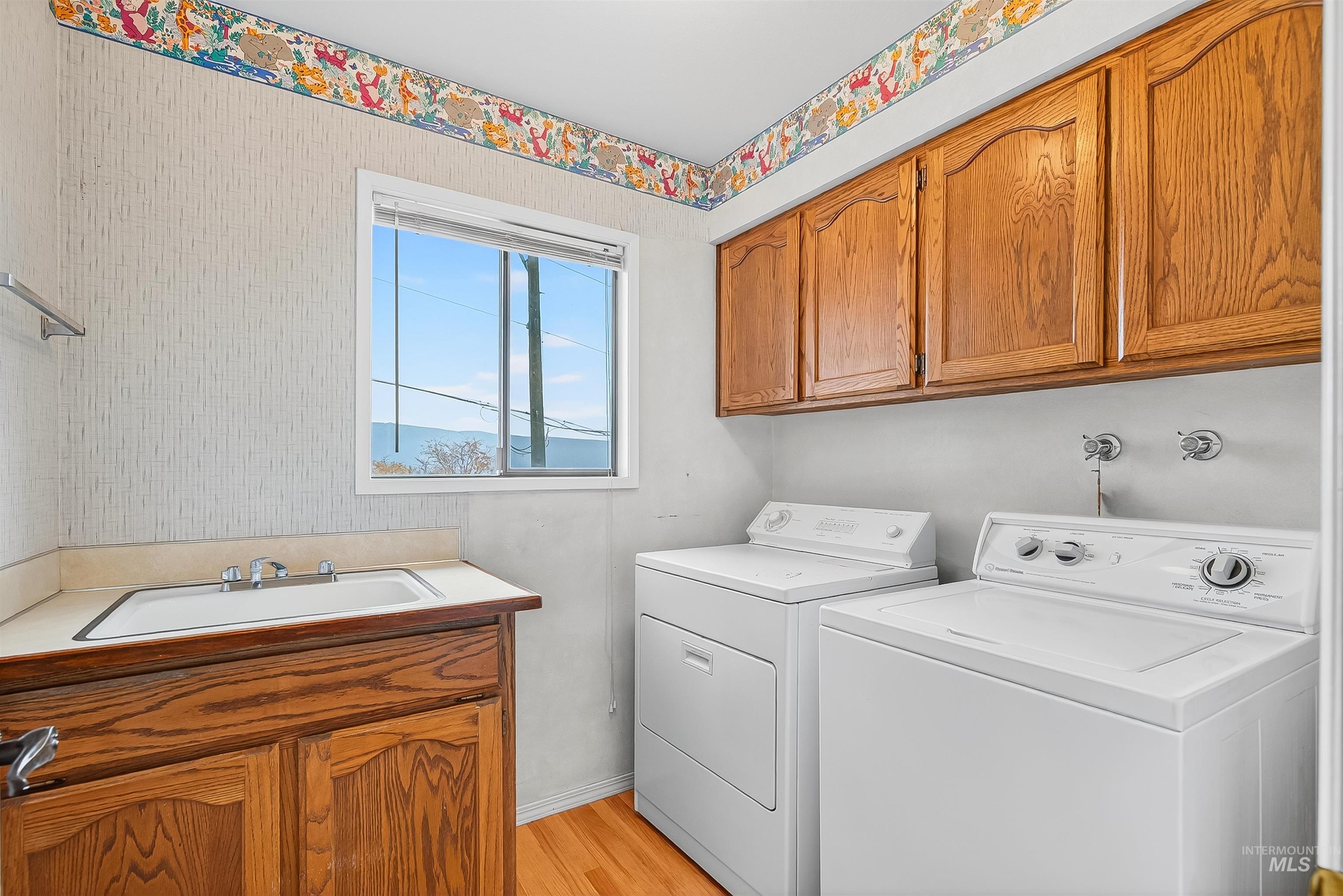 Laundry area featuring cabinet space, light wood-style flooring, washer and dryer, and wallpapered walls