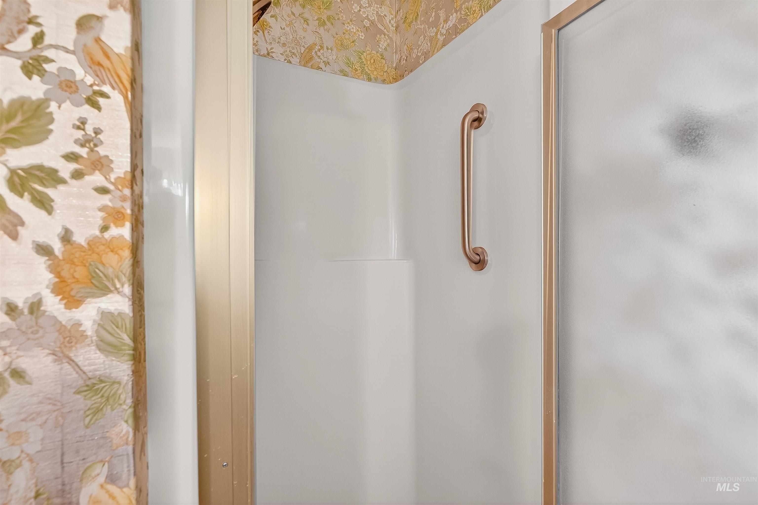 Bathroom view of a shower with shower door and wallpapered walls